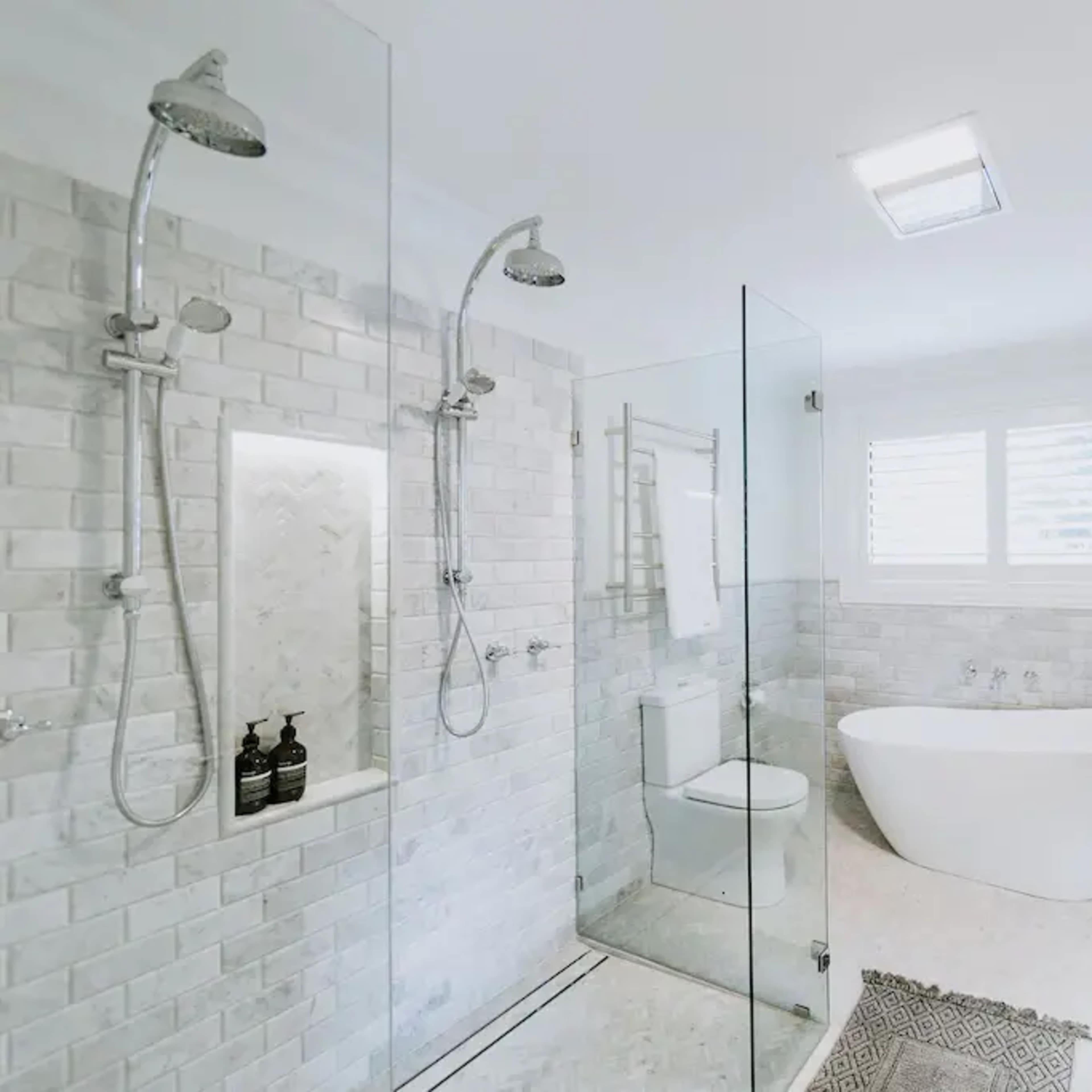 A modern bathroom featuring a glass-enclosed shower, a freestanding bathtub, a white vanity with a marble countertop, and a large round mirror.