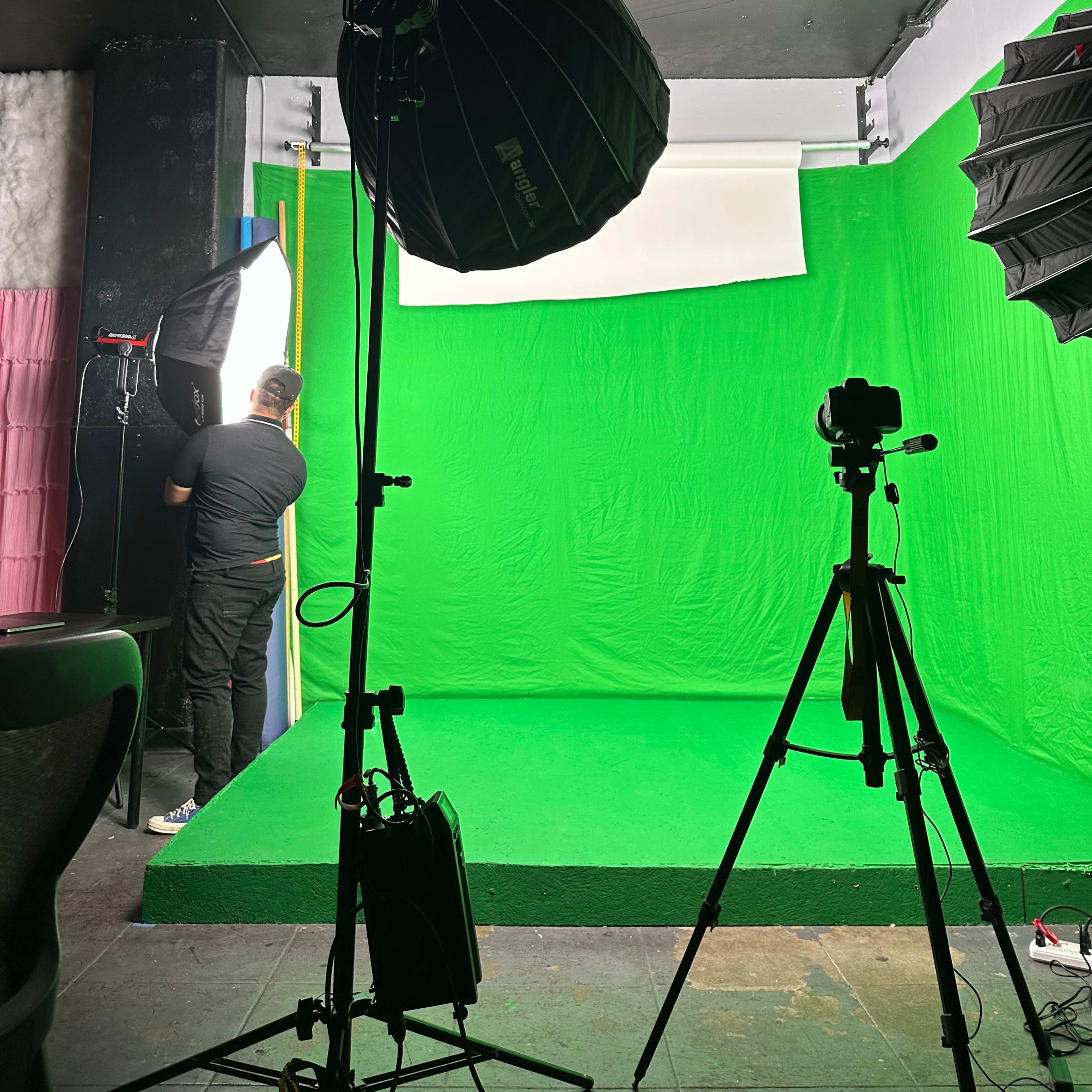 A green screen studio is set up with lighting equipment and a camera on a tripod.