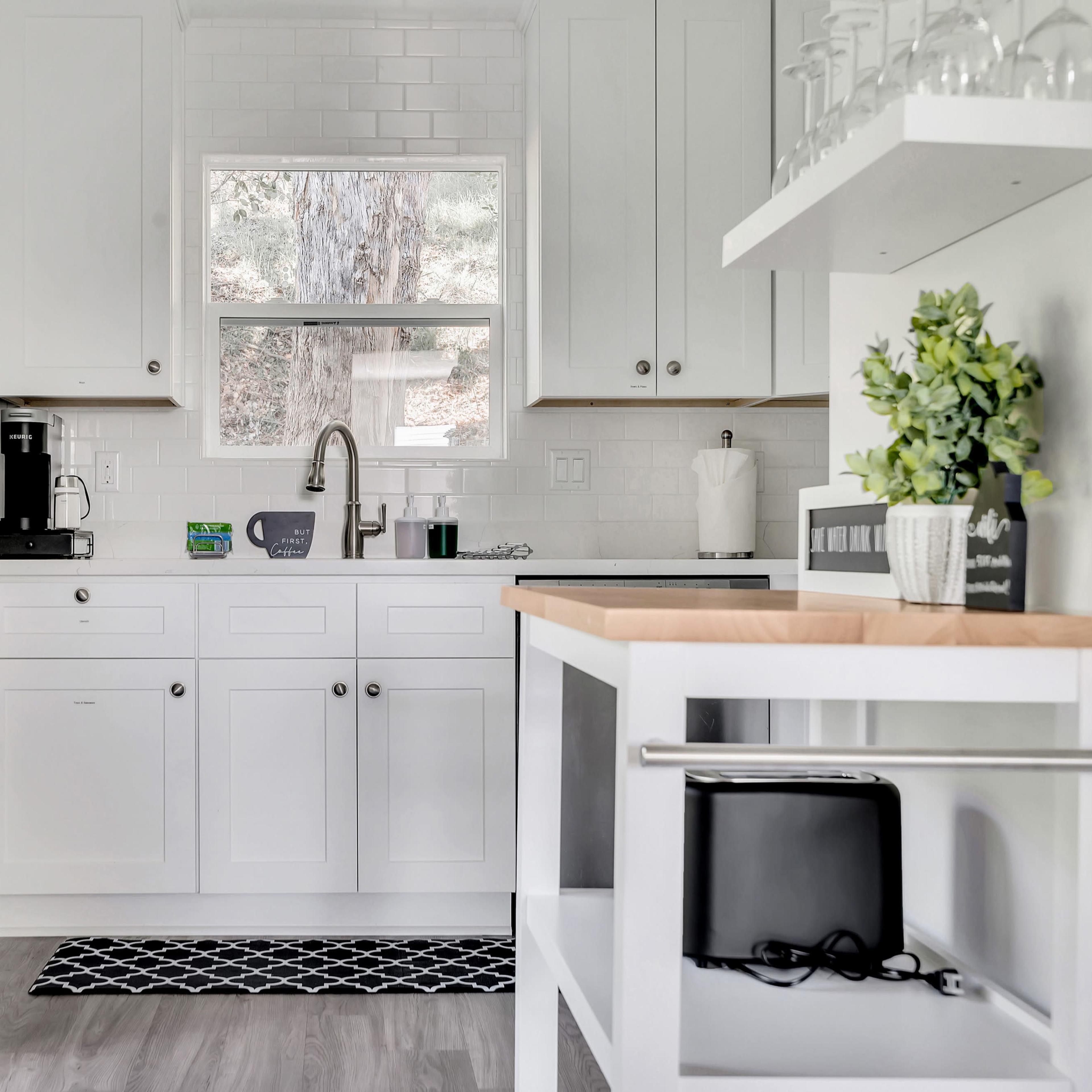 A modern kitchen features white cabinetry, stainless steel appliances, and a window overlooking a wooded area.