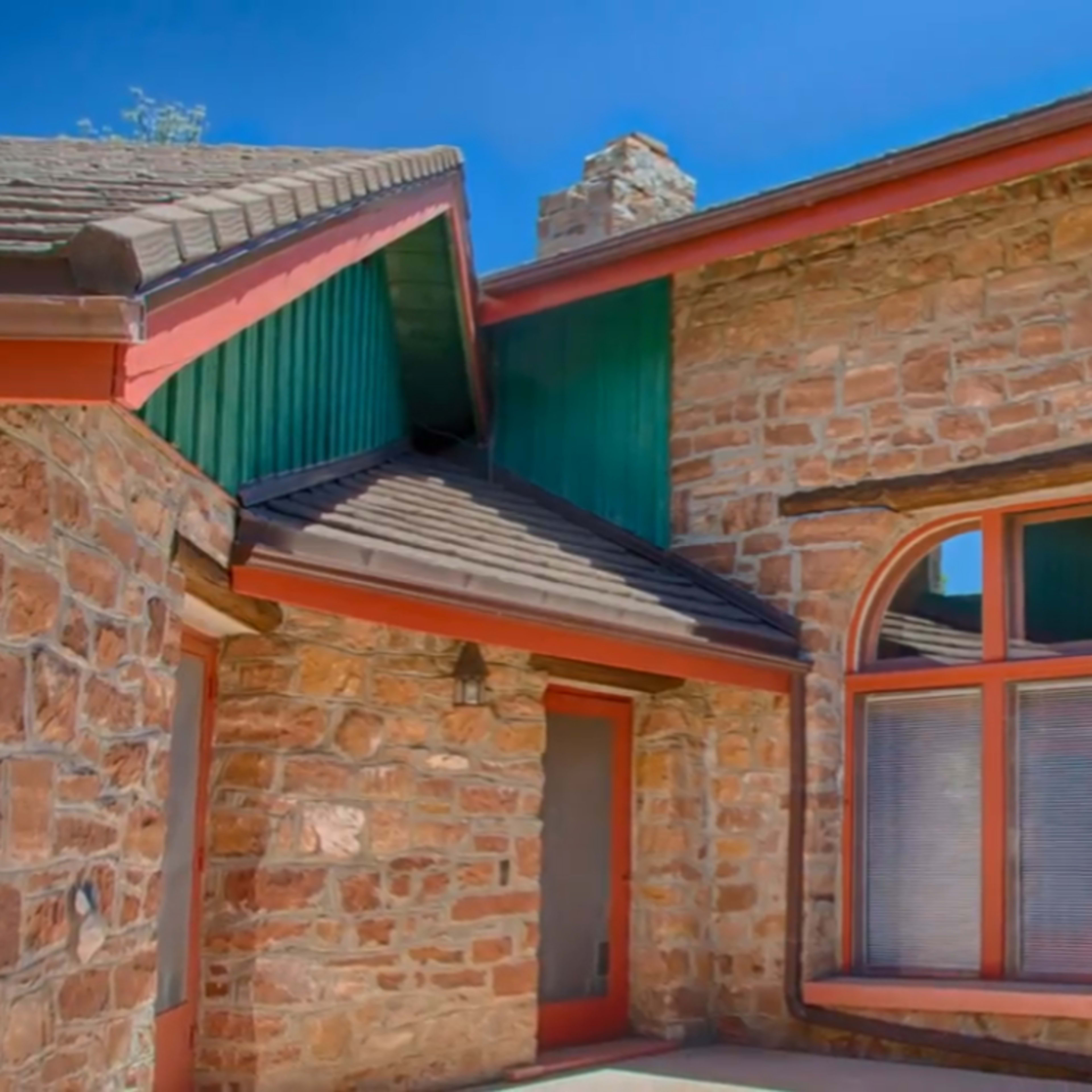 A stone house featuring a distinct angular design, large windows, and a combination of green and orange trim.