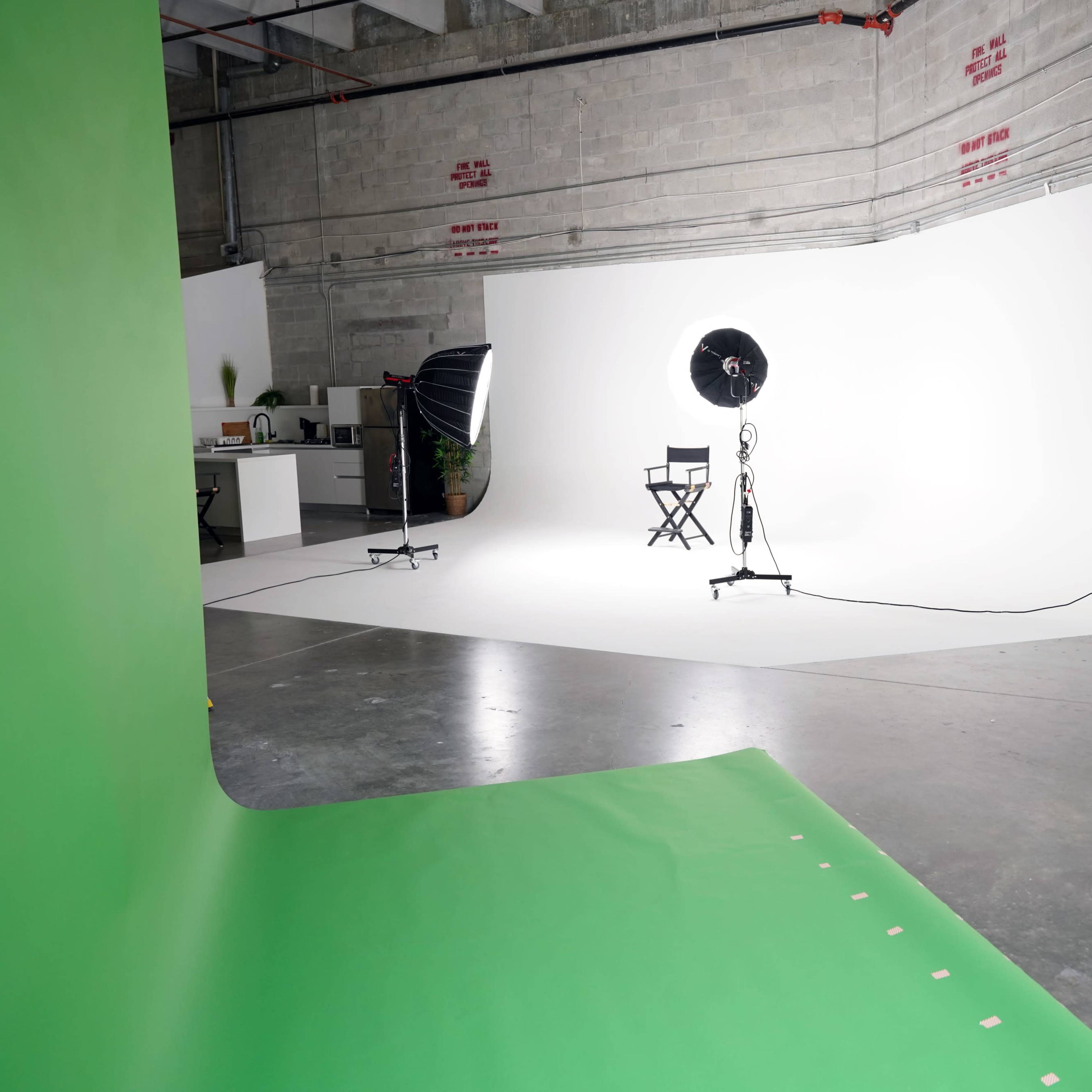 A photography studio with a green backdrop on one side and a white backdrop opposite, featuring a director's chair and lighting equipment.