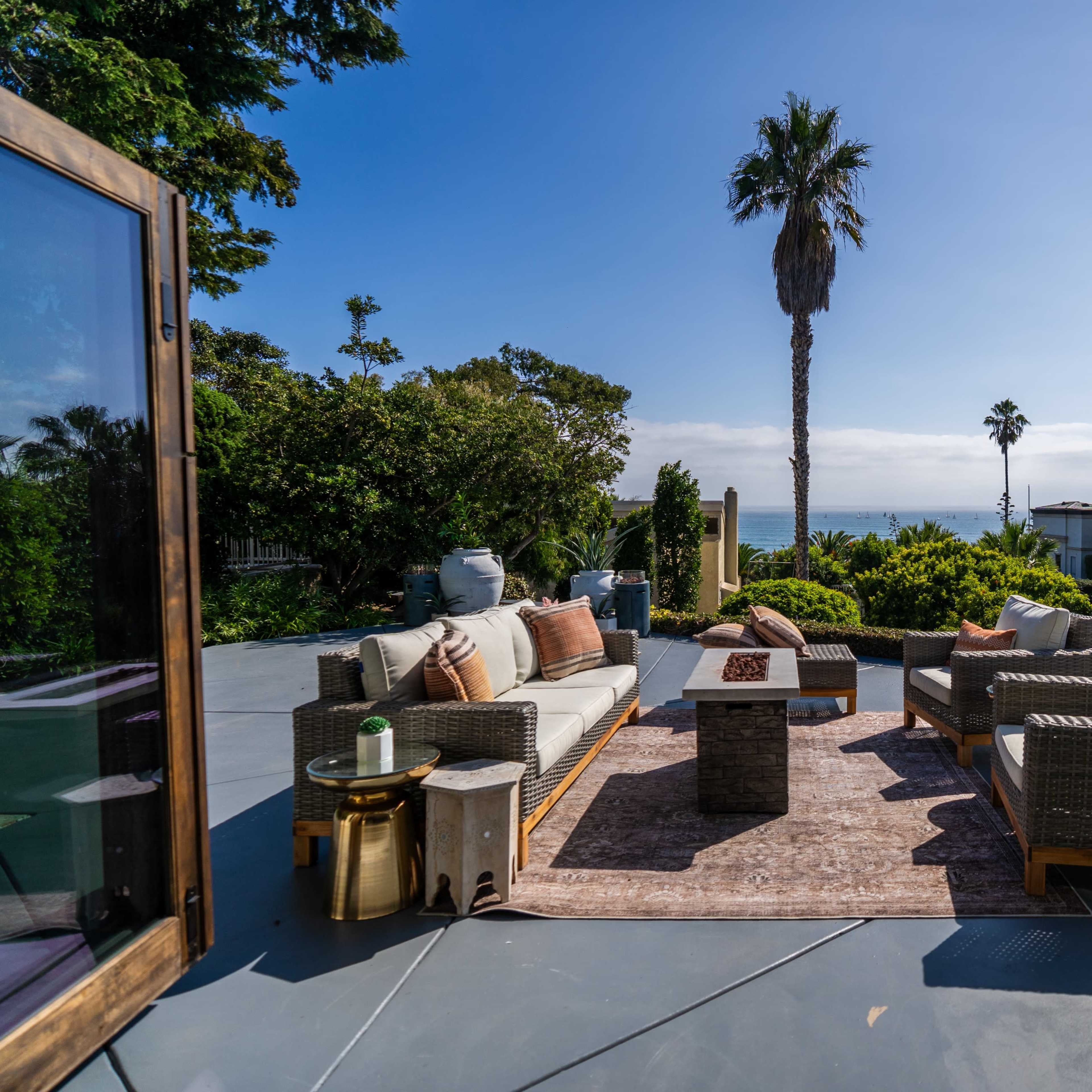 A spacious outdoor seating area with wicker furniture and a view of the ocean surrounded by tropical greenery.