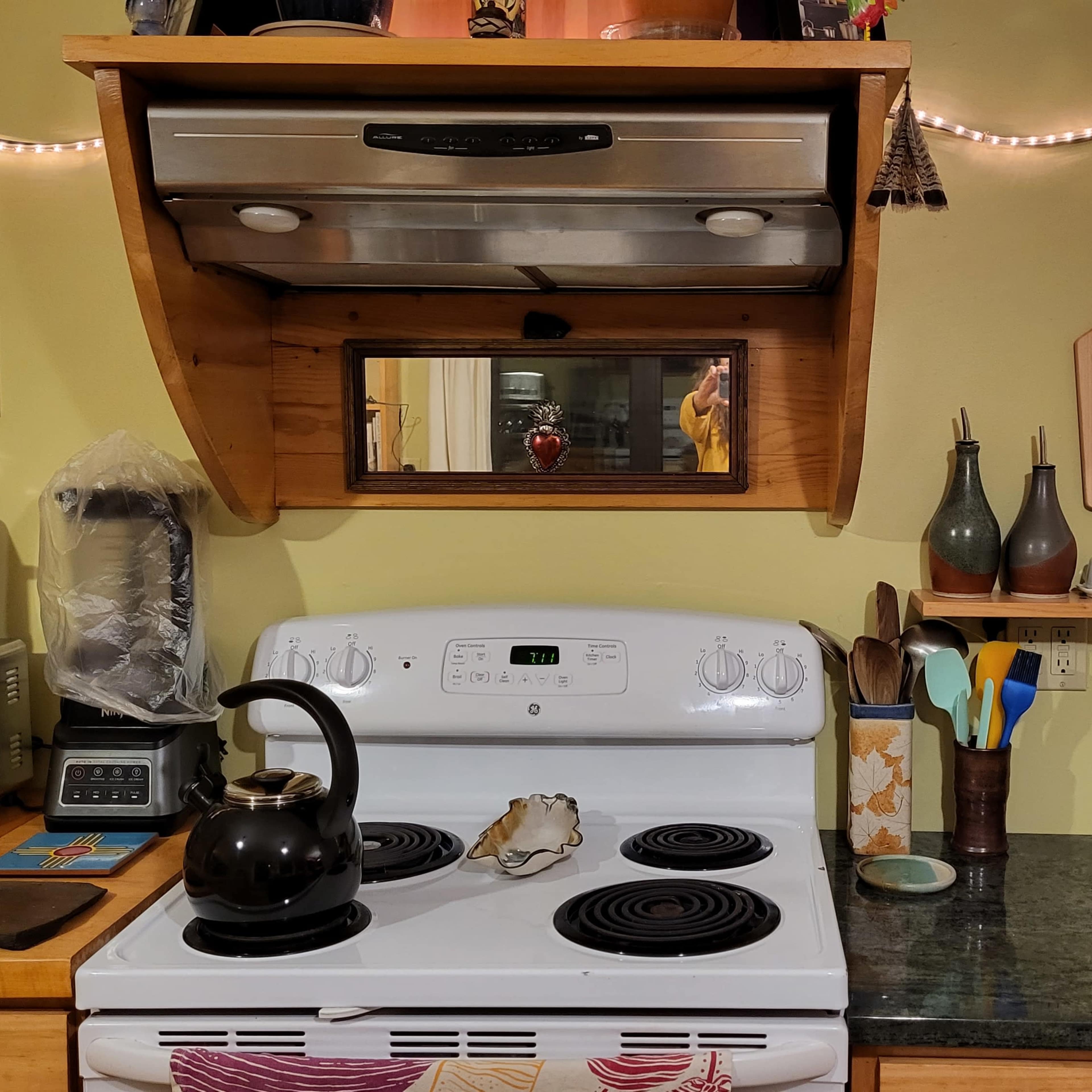 A kitchen with a stove, a kettle on the burner, and various kitchen utensils and appliances on the counters.