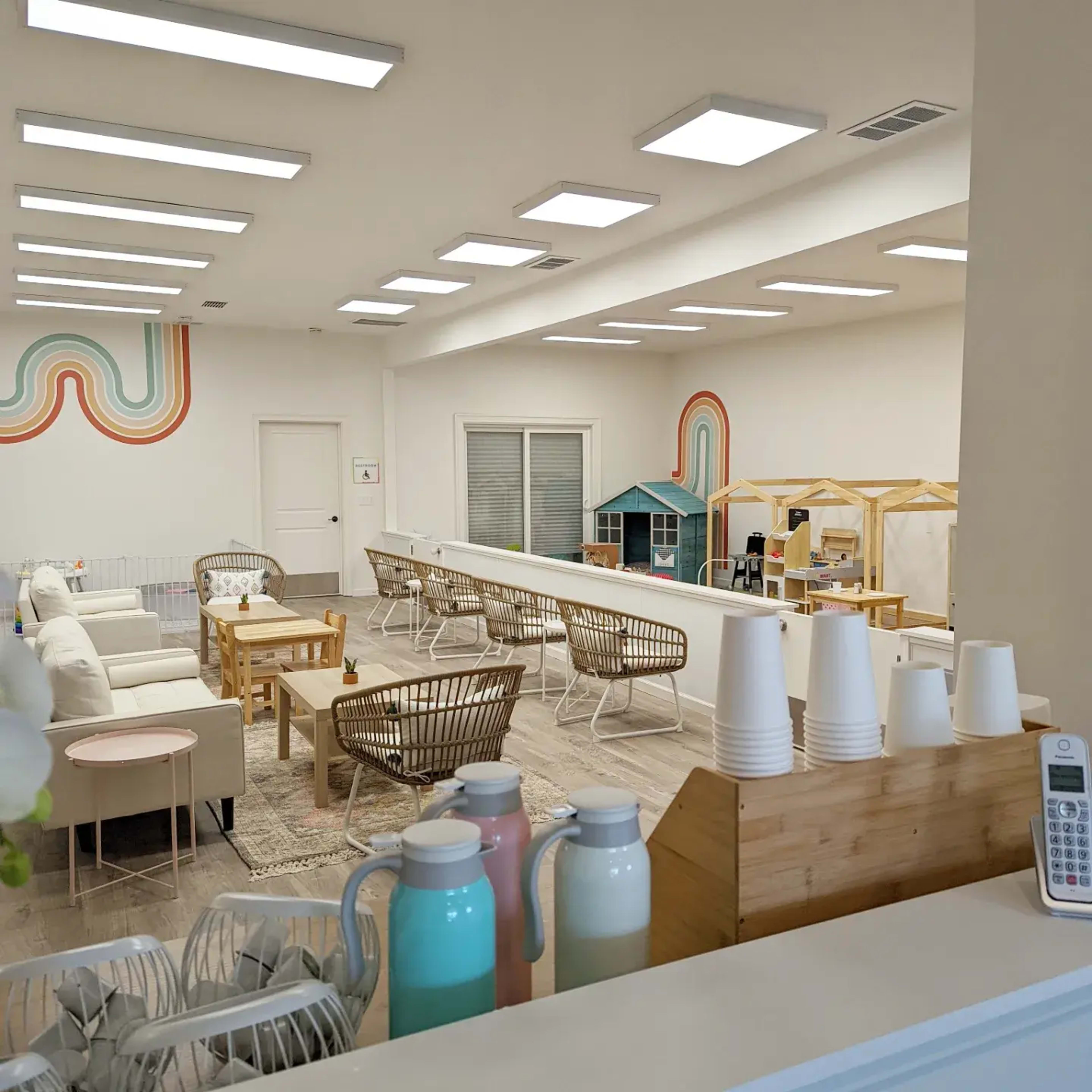 A bright, spacious room with various seating areas, colorful wall decorations, and play structures for children.
