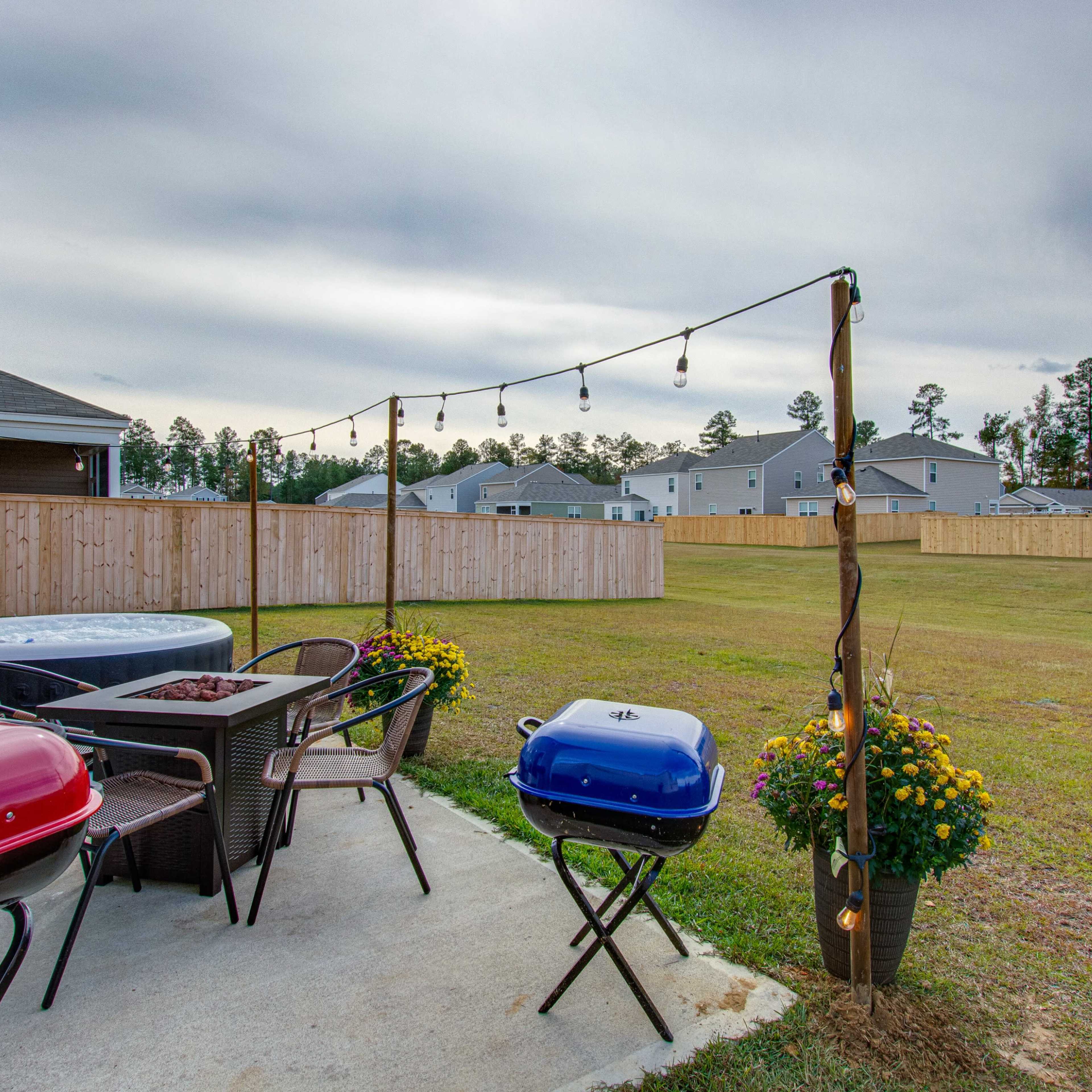 A backyard area features two grills and a seating arrangement, with string lights hanging above and a fenced yard in the background.