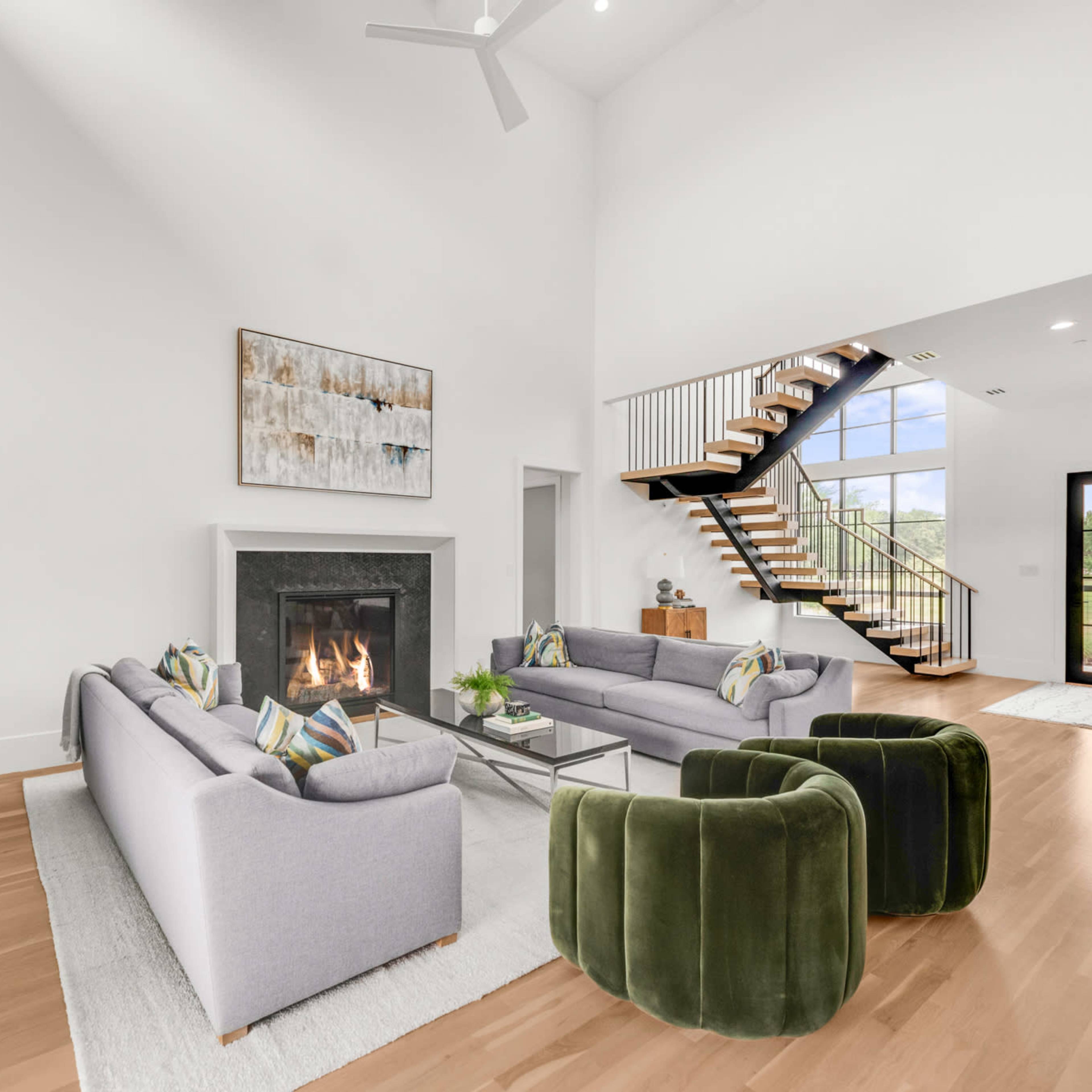 The spacious living room features a large fireplace, modern seating arrangements, and a staircase leading to an upper level.