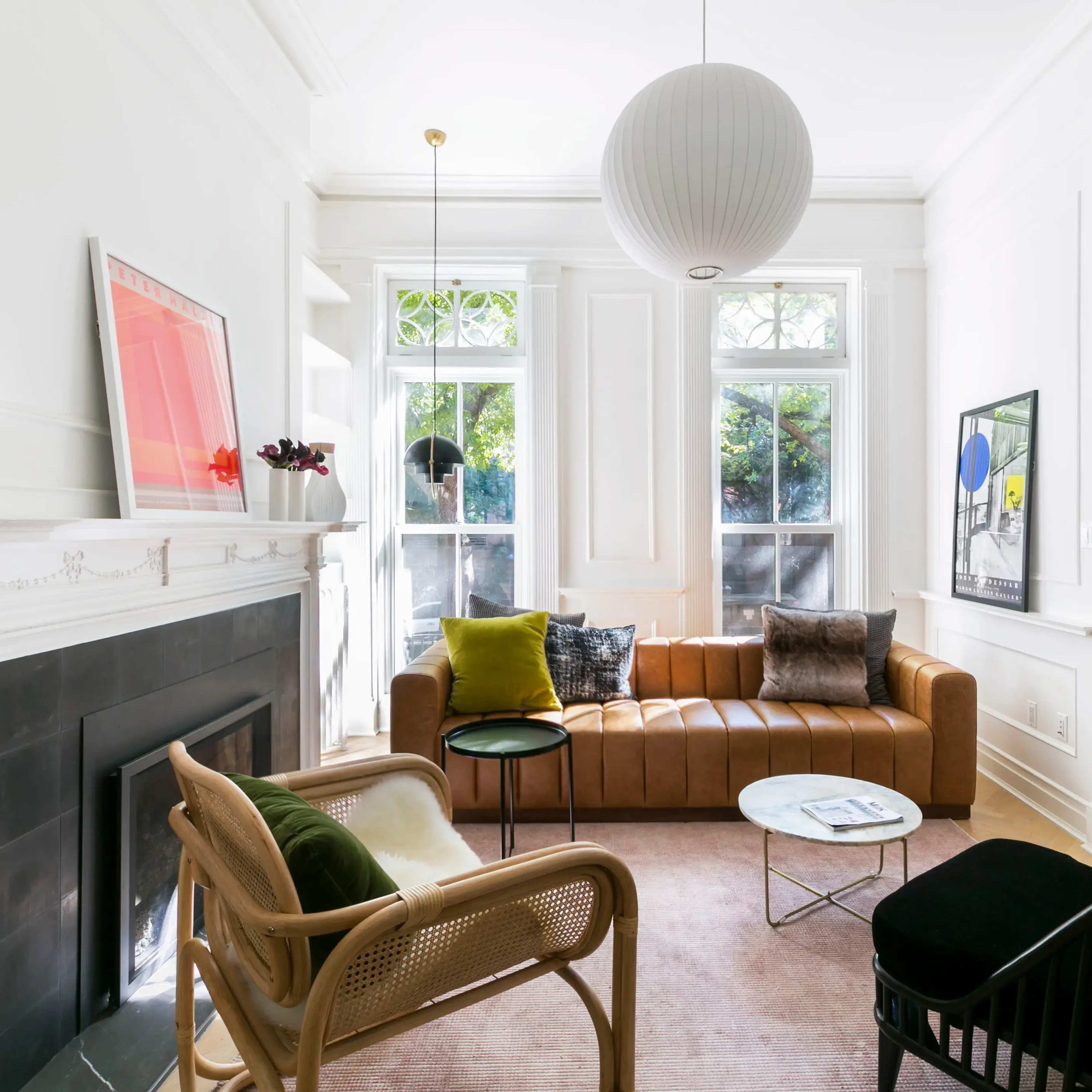 A modern living room features a brown leather sofa, a black accent chair, a round coffee table, and large windows with natural light.