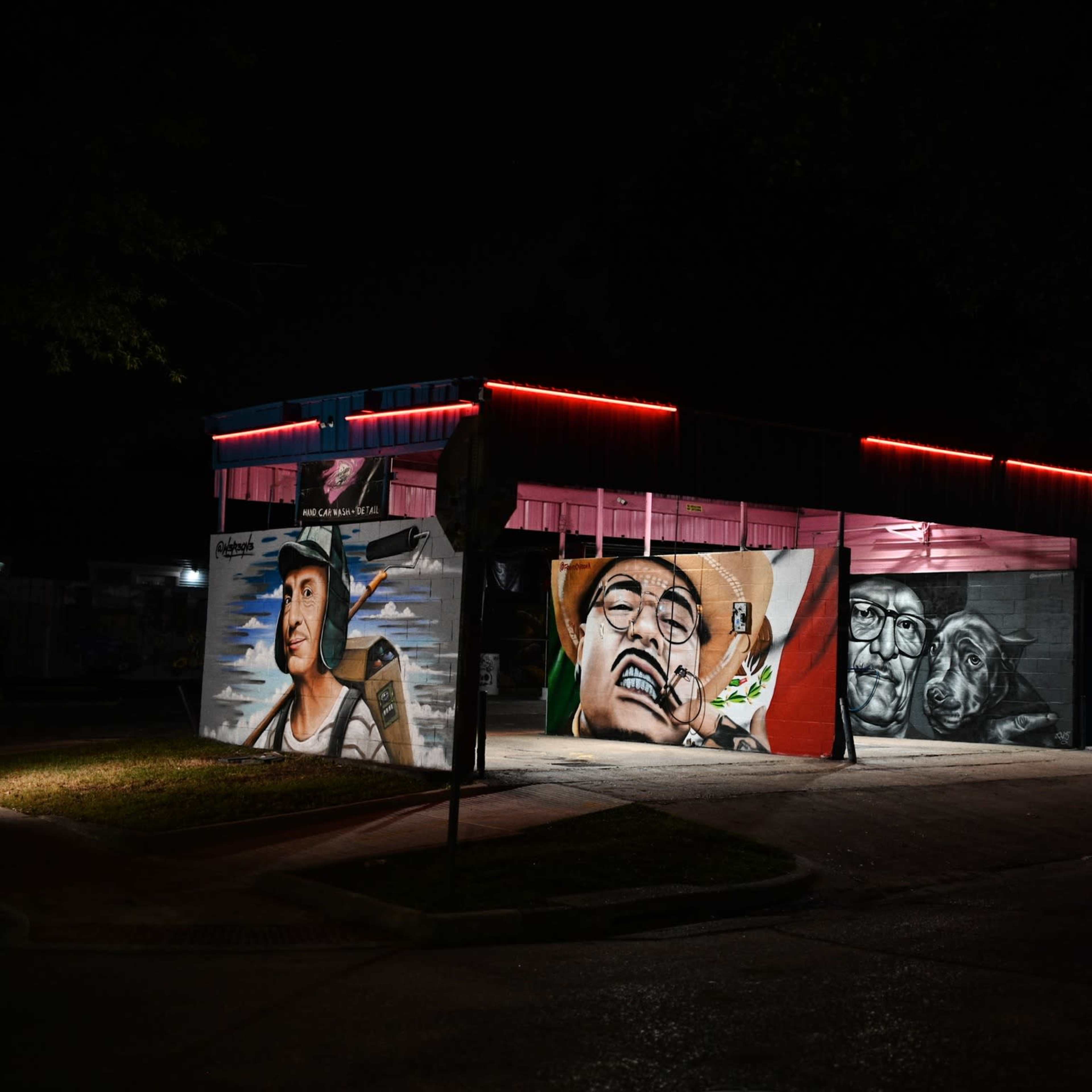A building at night displays vibrant murals on its exterior walls, highlighted by neon red lights.