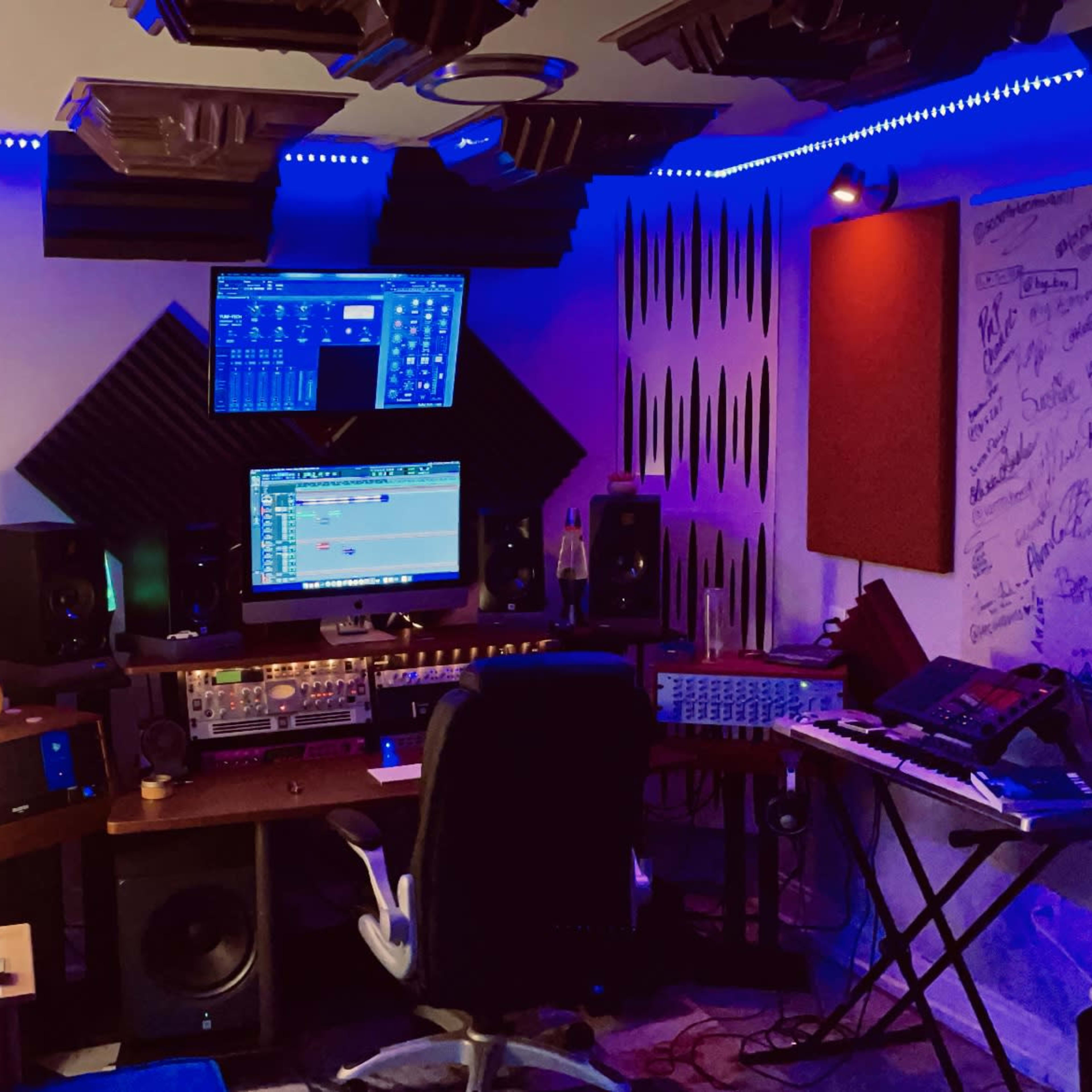 A music production studio equipped with multiple screens, audio equipment, and soundproofing panels on the walls.