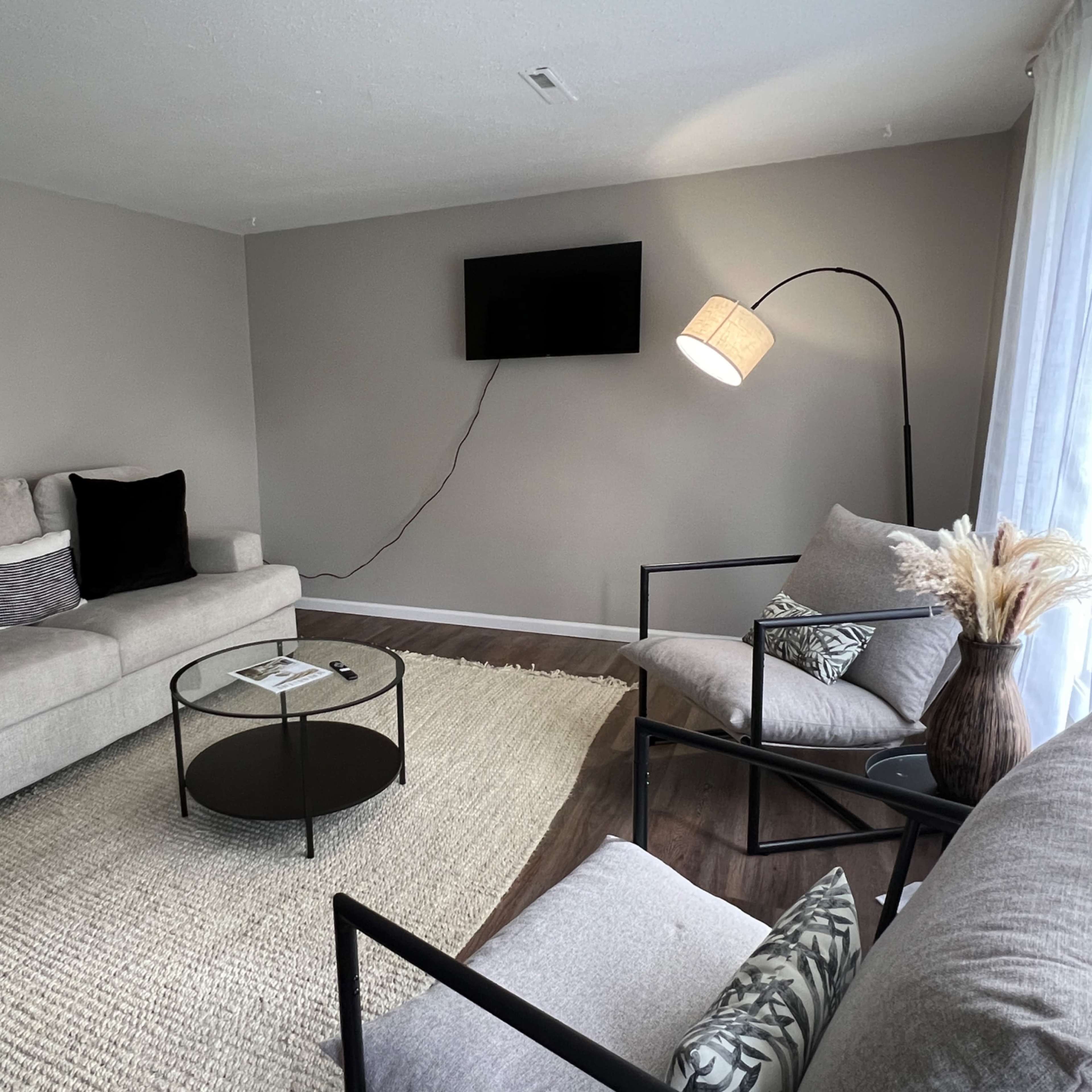 A living room with two sofas, a black coffee table, a floor lamp, and a television mounted on the wall.