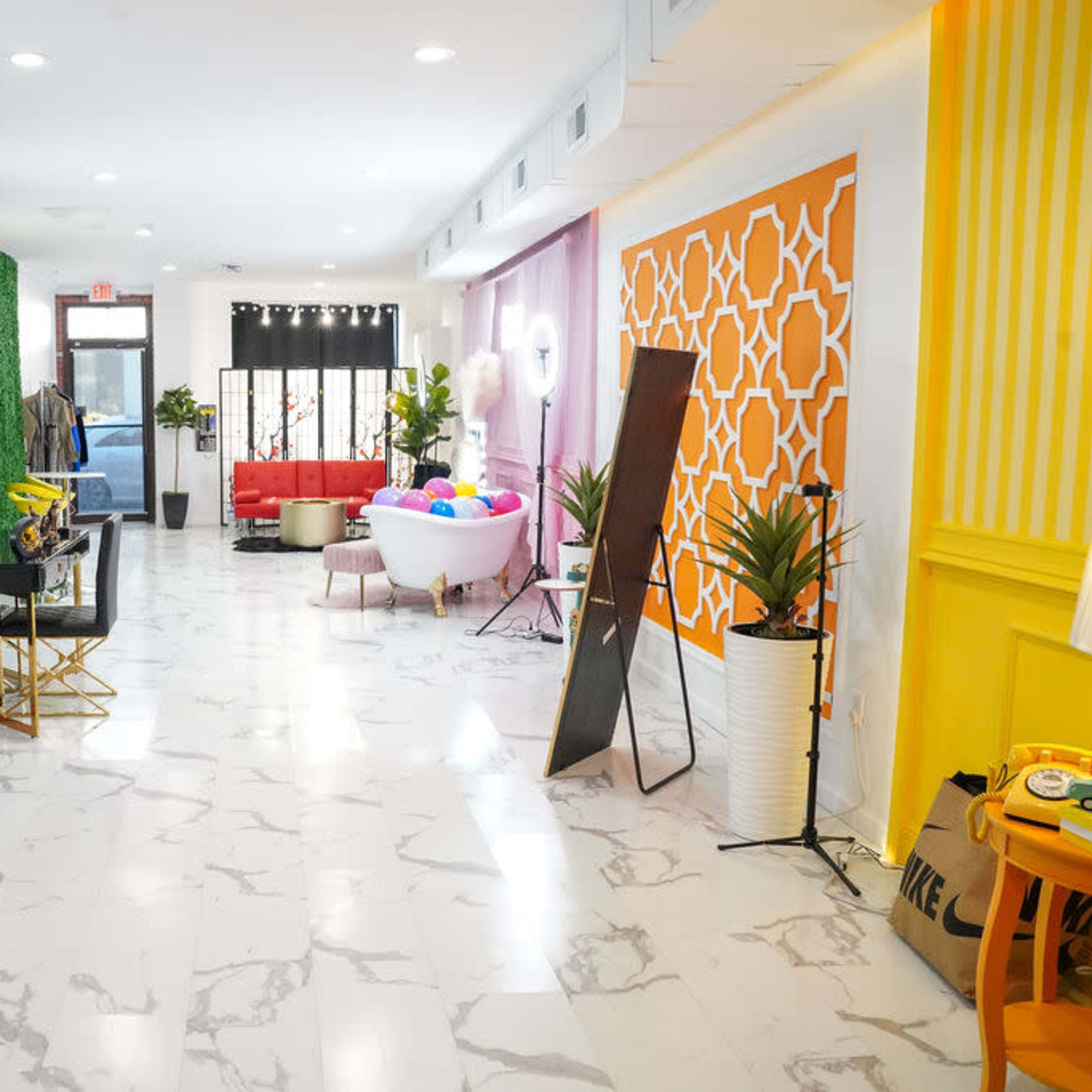 A brightly lit interior space with various colorful walls, modern furniture, and a mix of decorative elements, including plants and lighting setups.