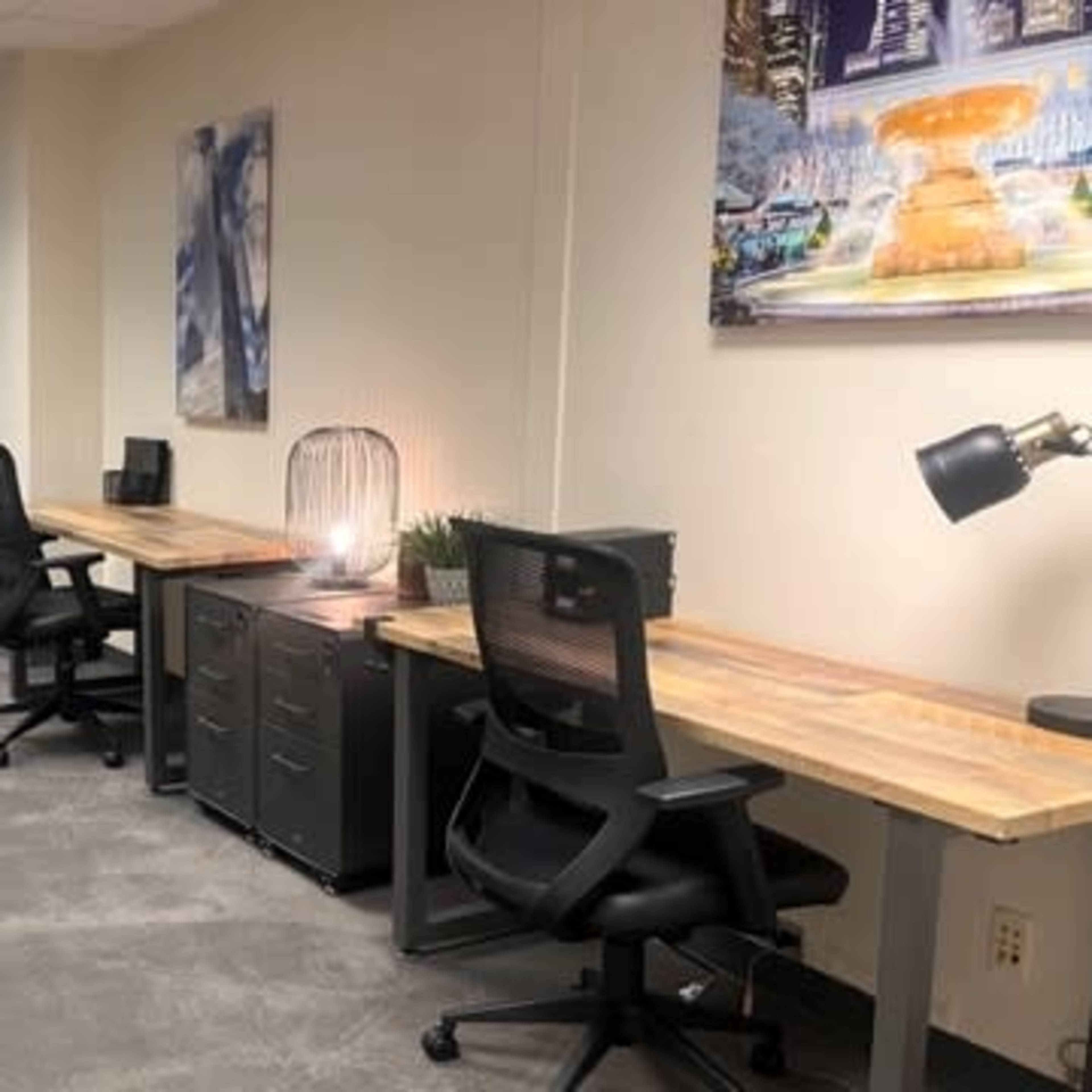 A modern office space featuring two wooden desks with chairs, a couch, and decorative wall art.