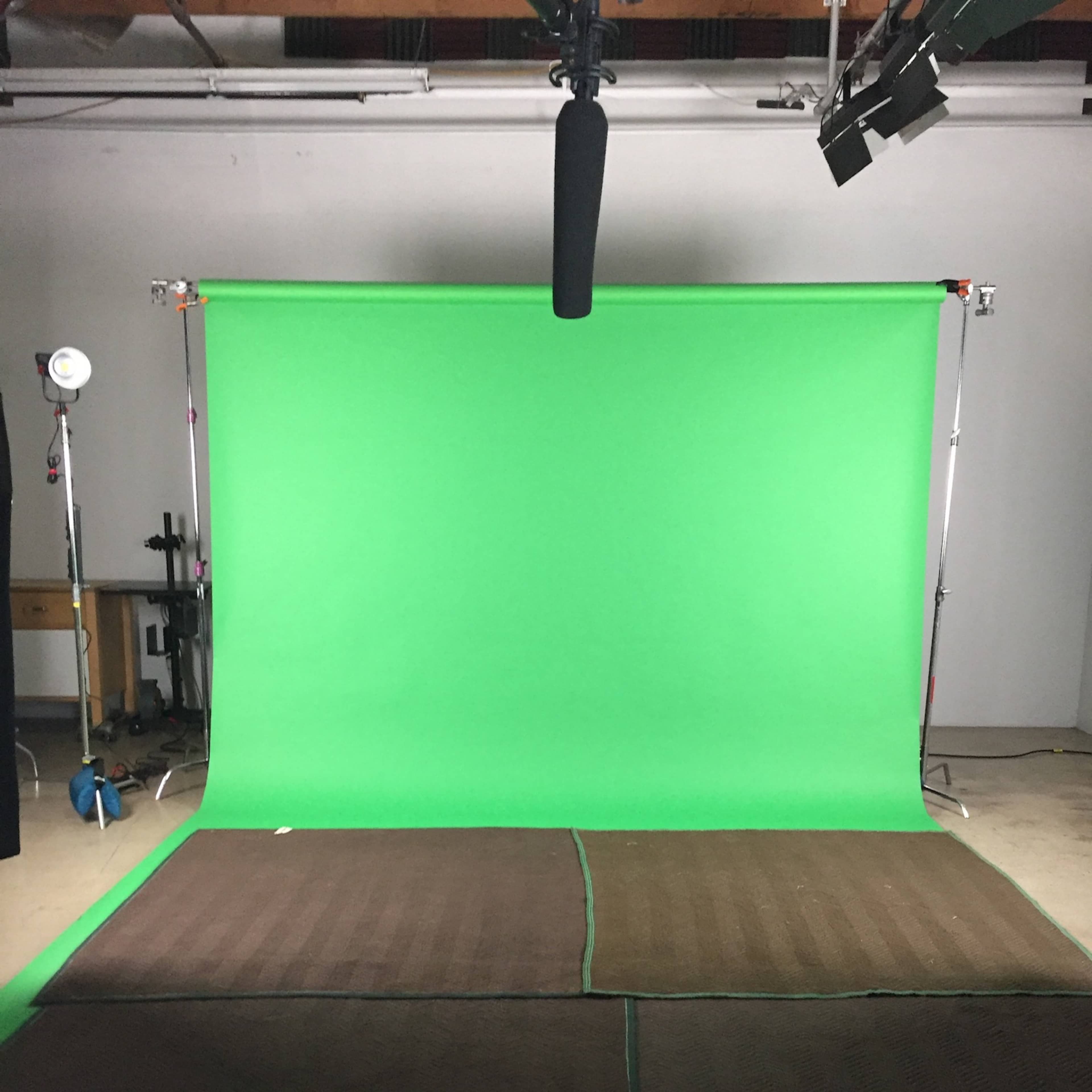 A green screen setup with lights and a microphone overhead in a studio space.