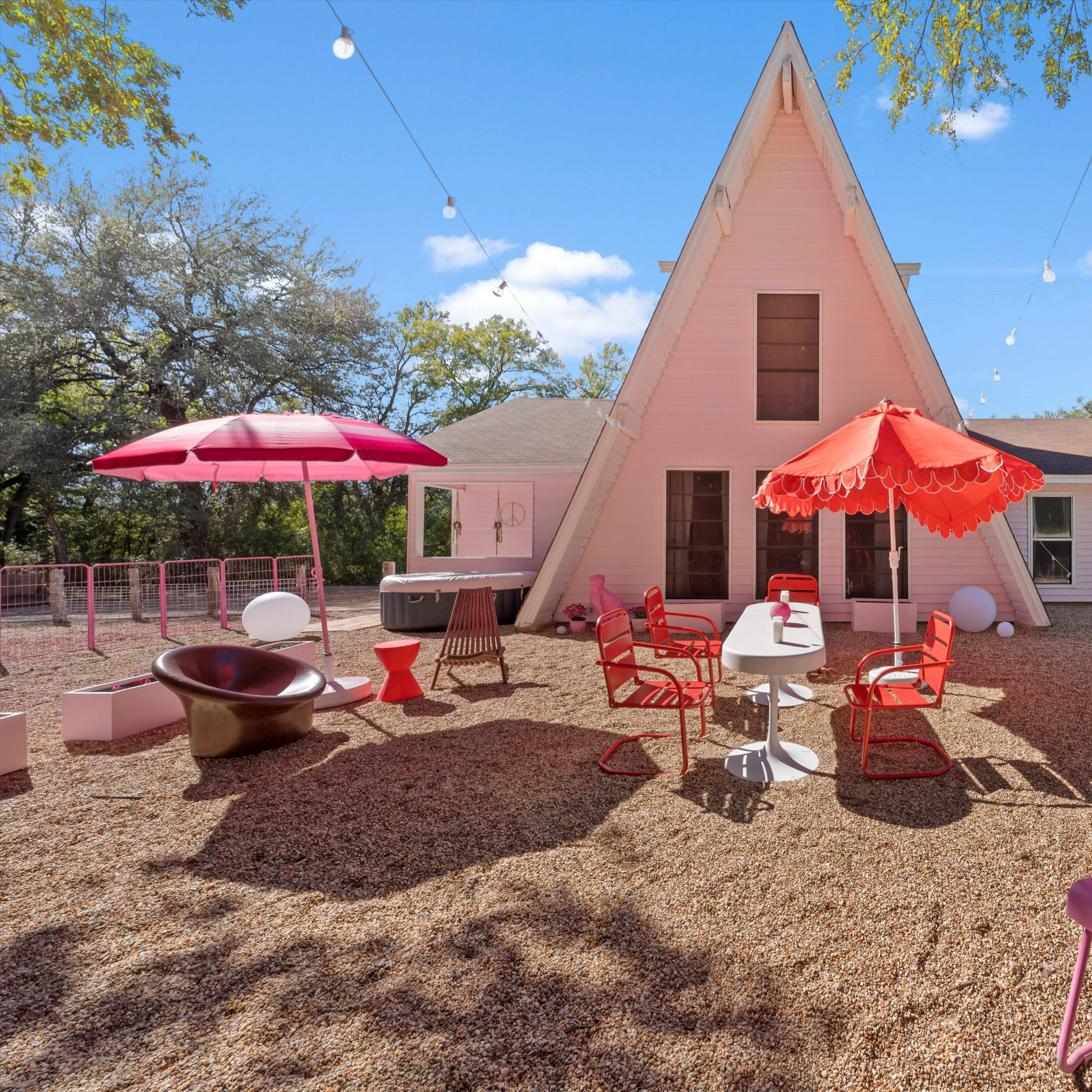 A modern A-frame house with a gravel patio features colorful outdoor furniture and decorative lighting strung above.