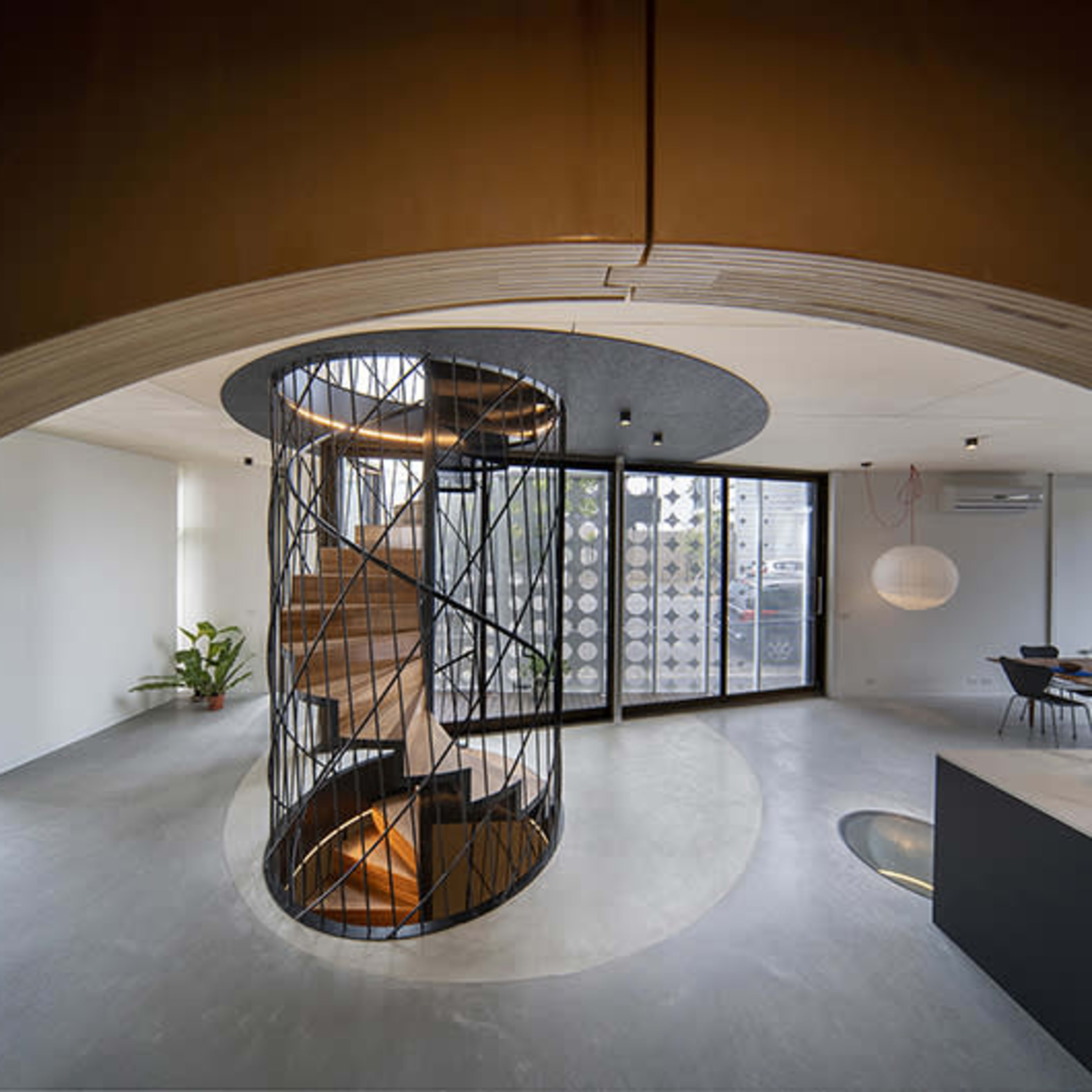 A modern interior space with a spiral staircase at its center, surrounded by large windows and minimalist furniture.