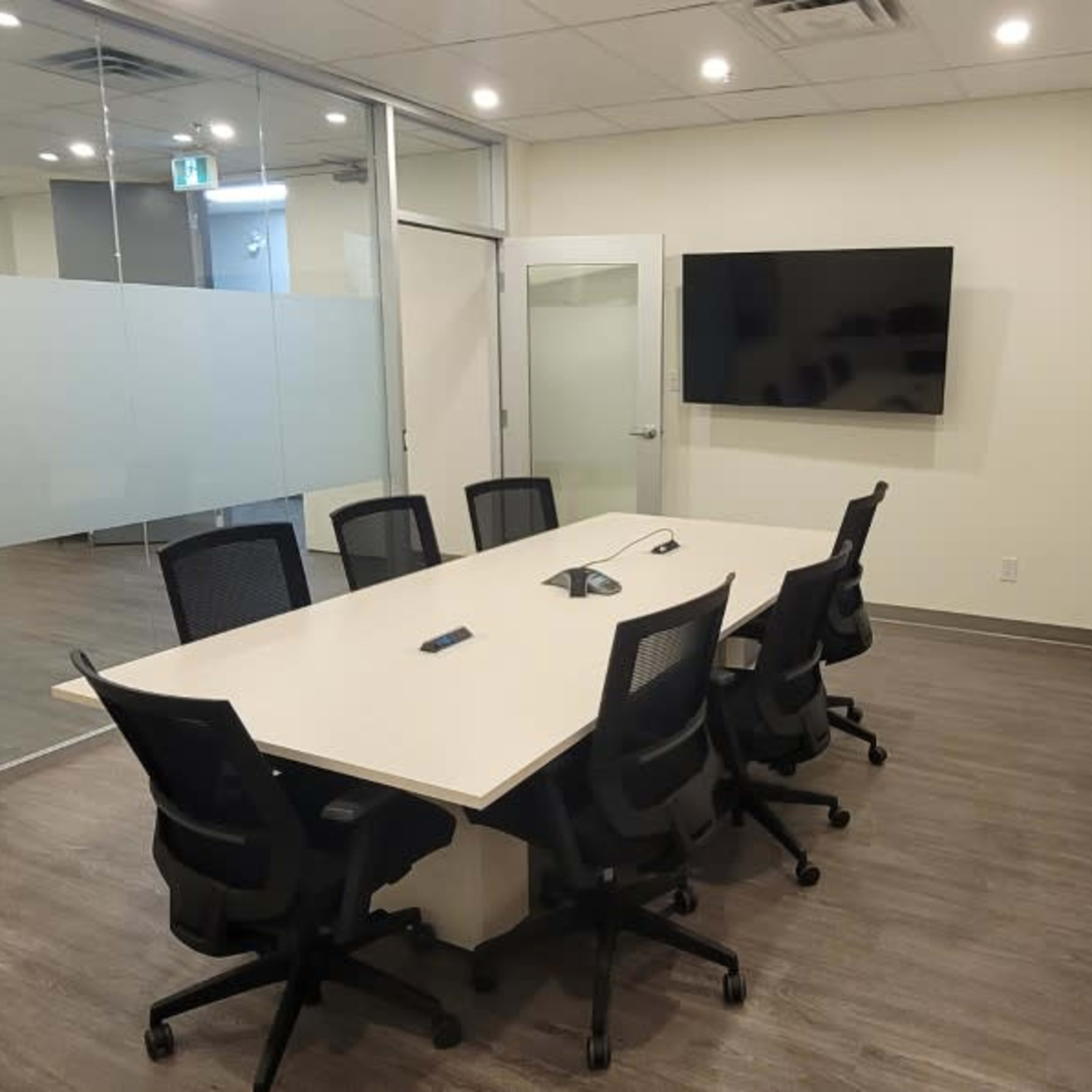 A modern conference room with a long table, several black chairs, and multiple wall-mounted screens.