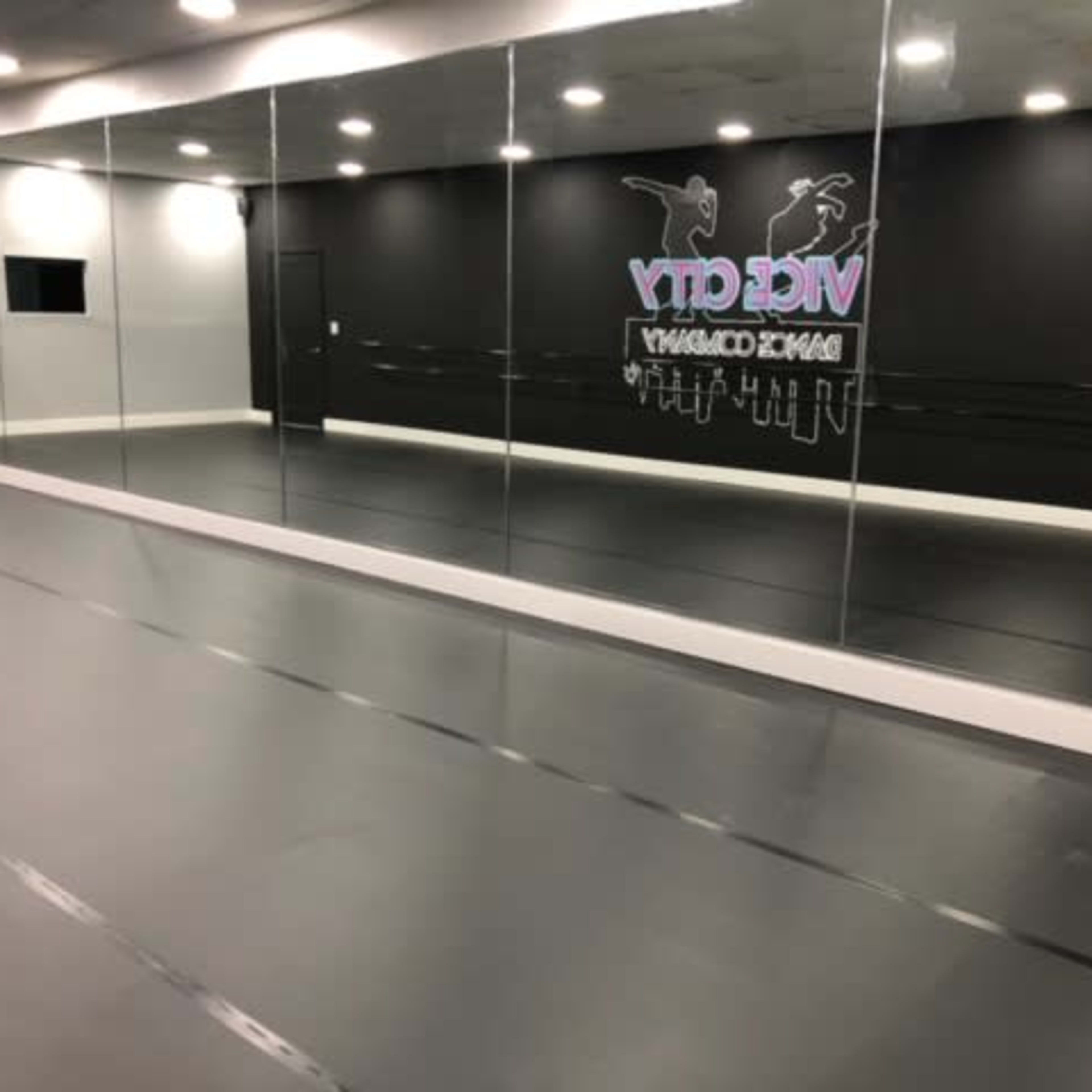 A dance studio with mirrored walls, a black backdrop, and a smooth gray floor.