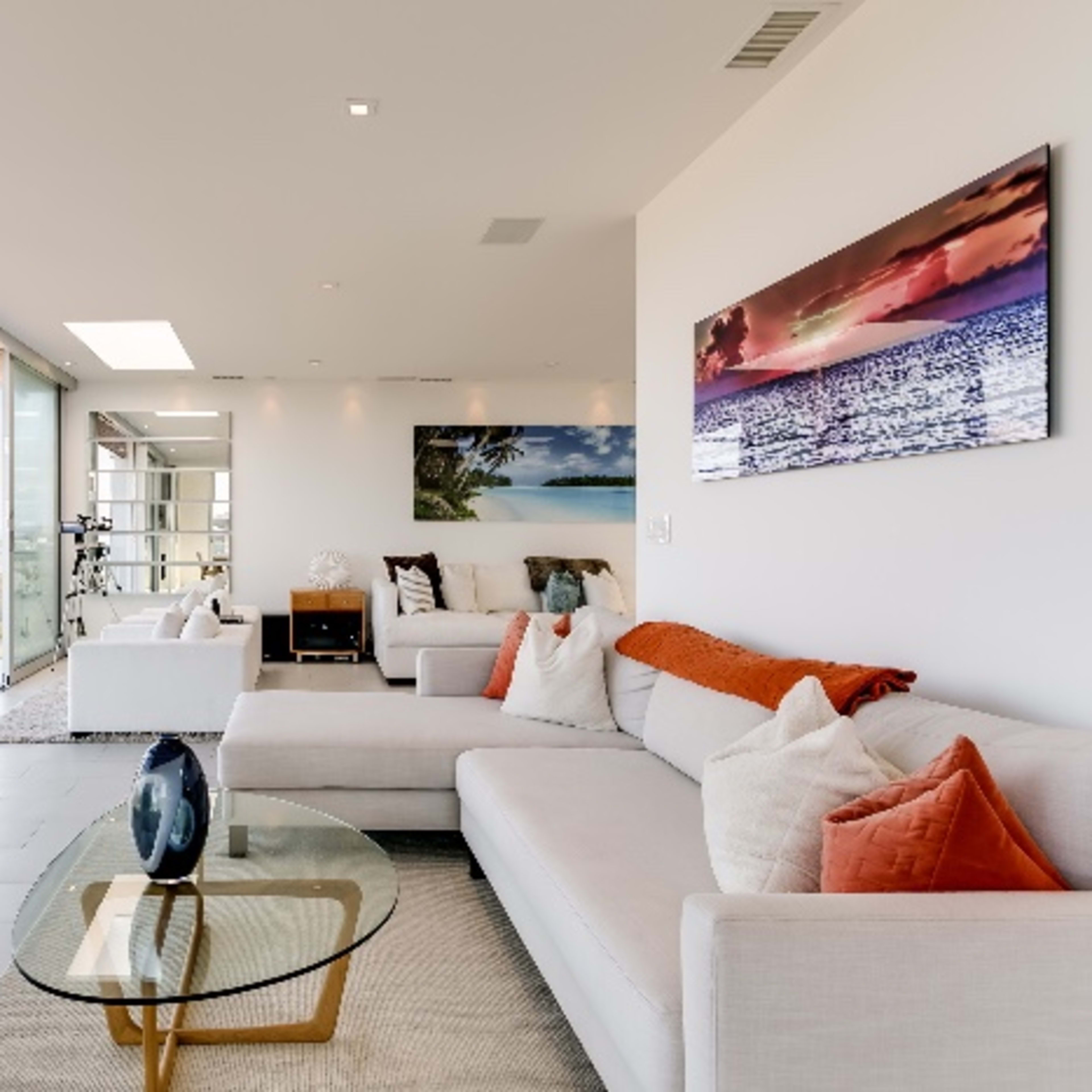 A modern living room with large glass windows overlooking a landscape, featuring light-colored sofas, a round glass coffee table, and minimal decor.