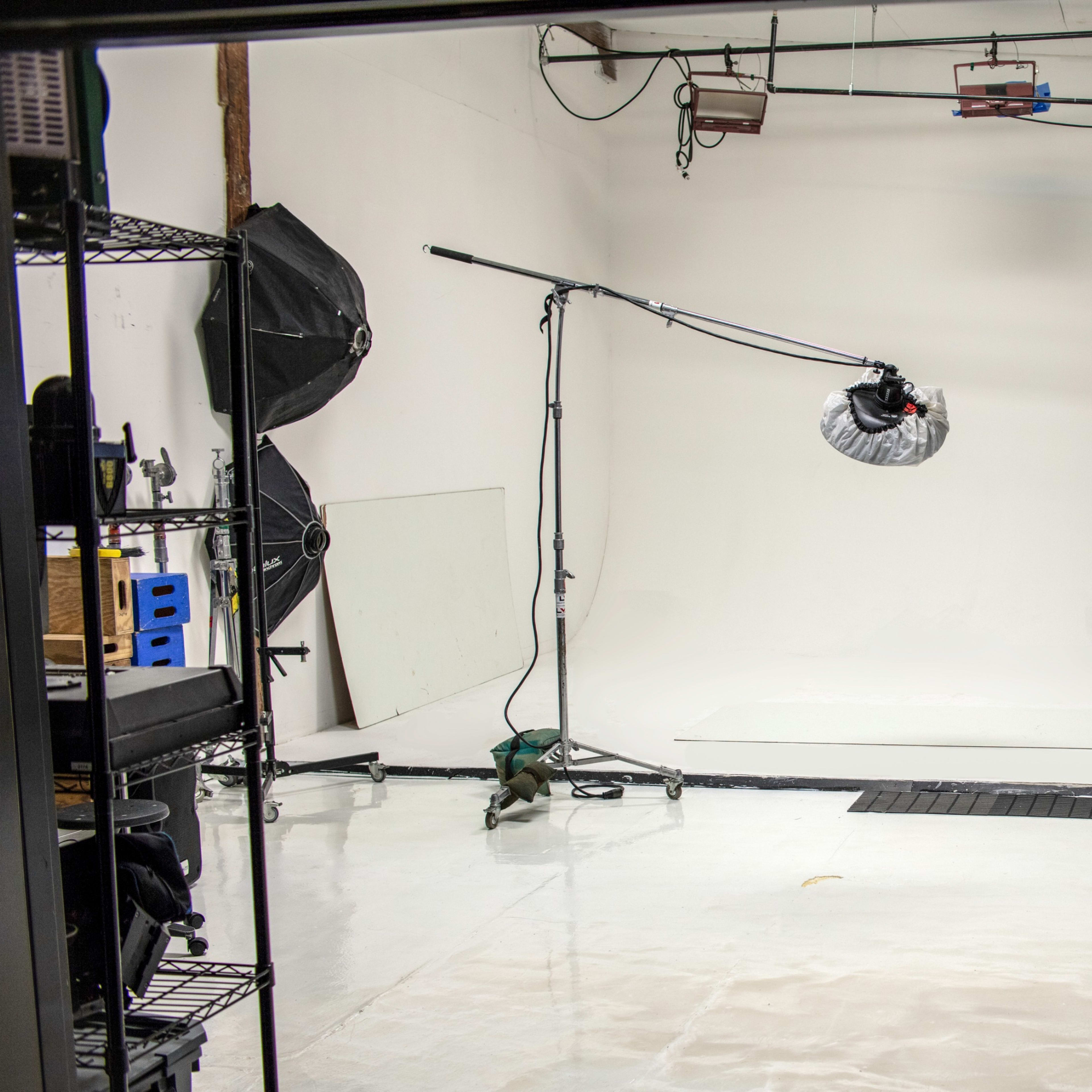 A photography studio with a white backdrop, lighting equipment, and various props arranged along the sides.