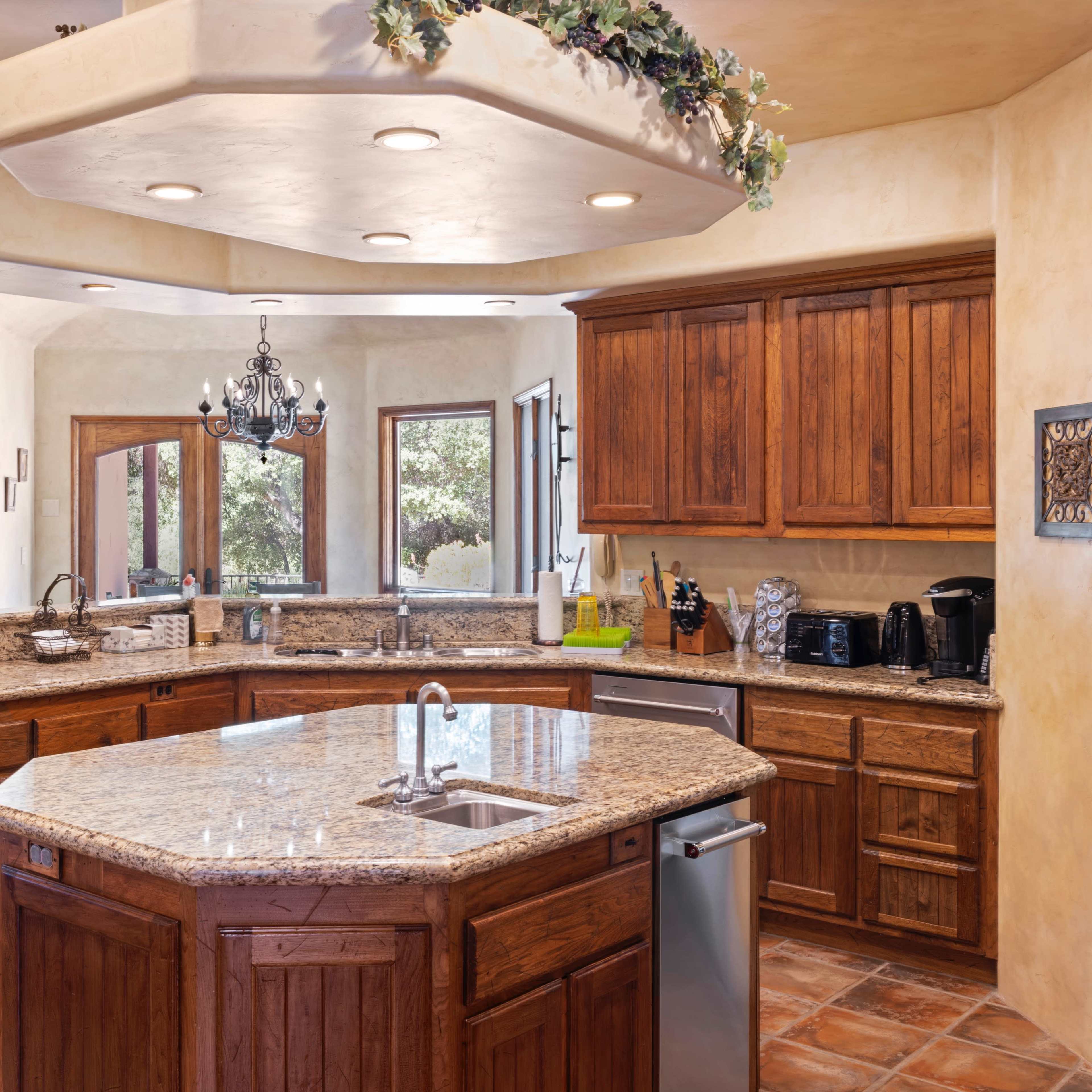 A spacious kitchen with wooden cabinetry, a large granite island, and multiple windows allowing natural light to enter.