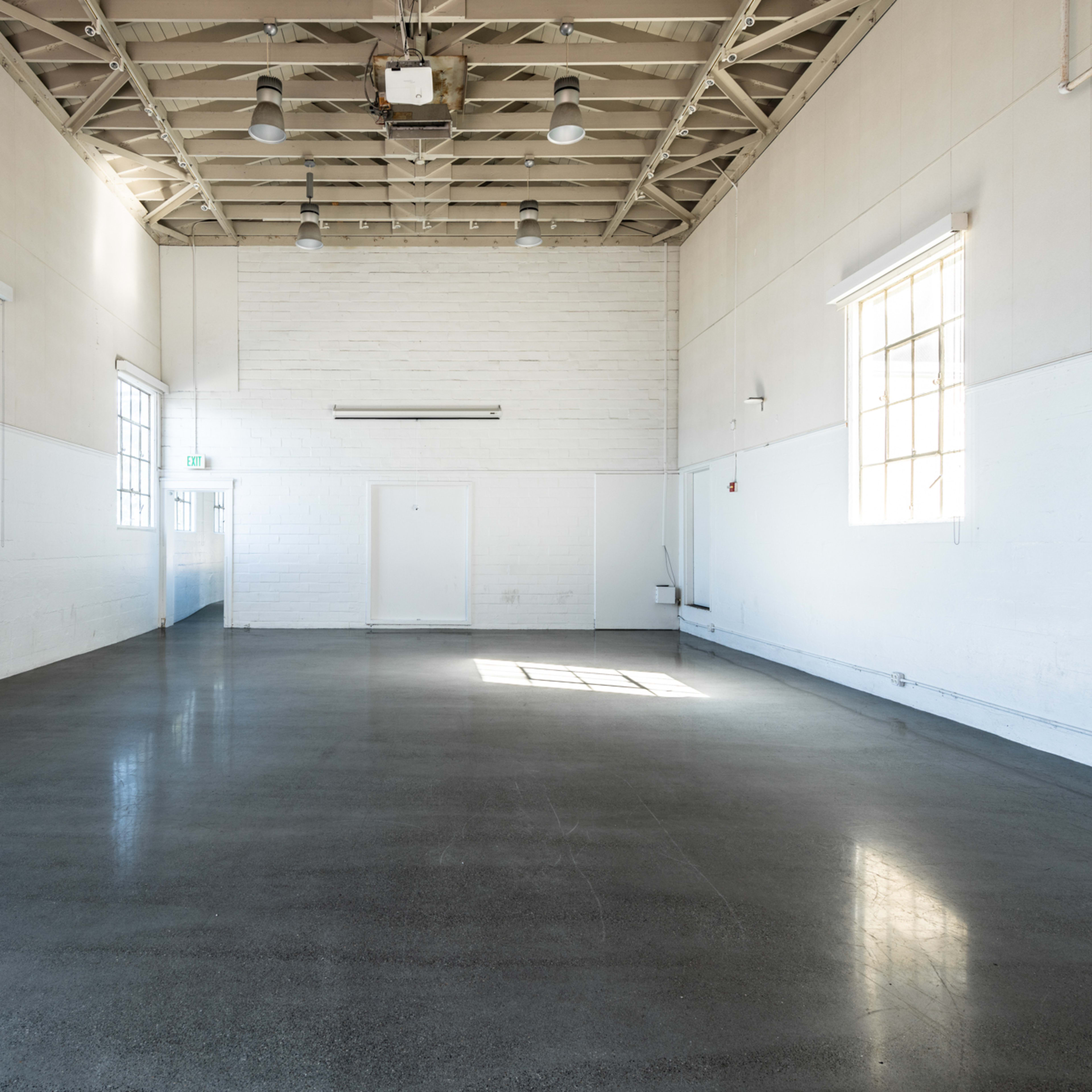 An empty, spacious room features large windows on two walls and a polished concrete floor.