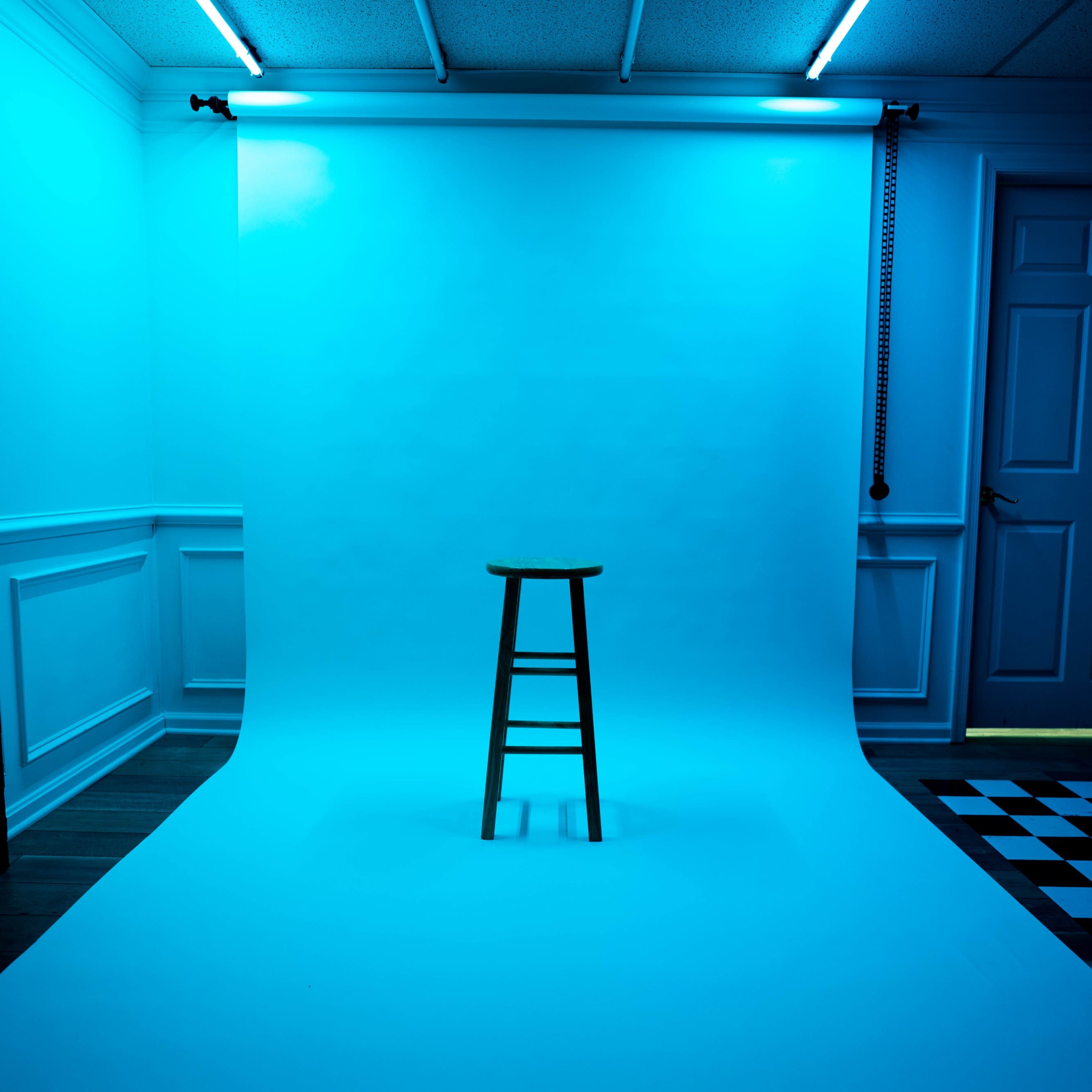 A wooden stool is positioned in front of a blue backdrop in a dimly lit studio.