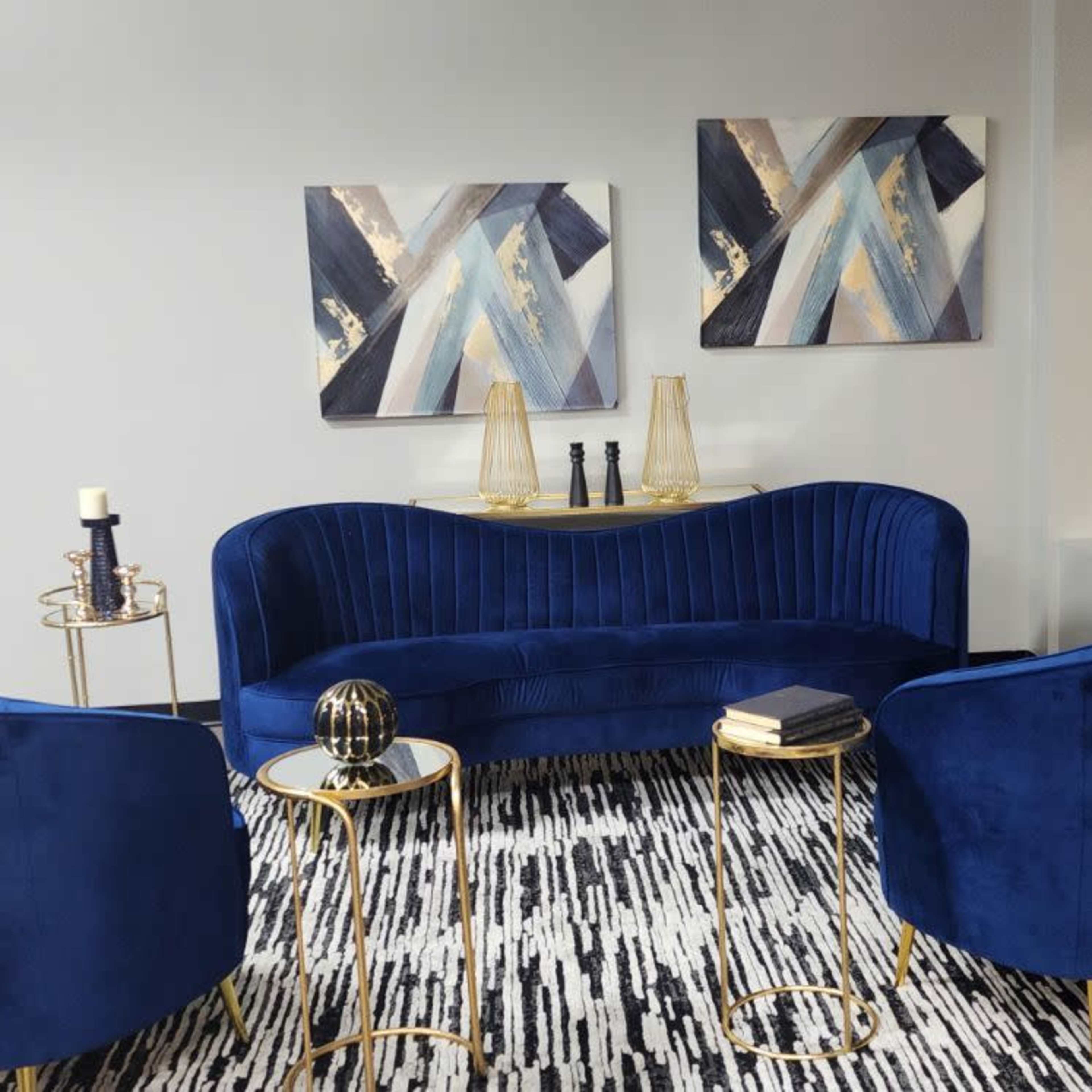 A modern lounge area features a blue velvet sofa and two matching armchairs arranged around a circular gold side table on a patterned rug.
