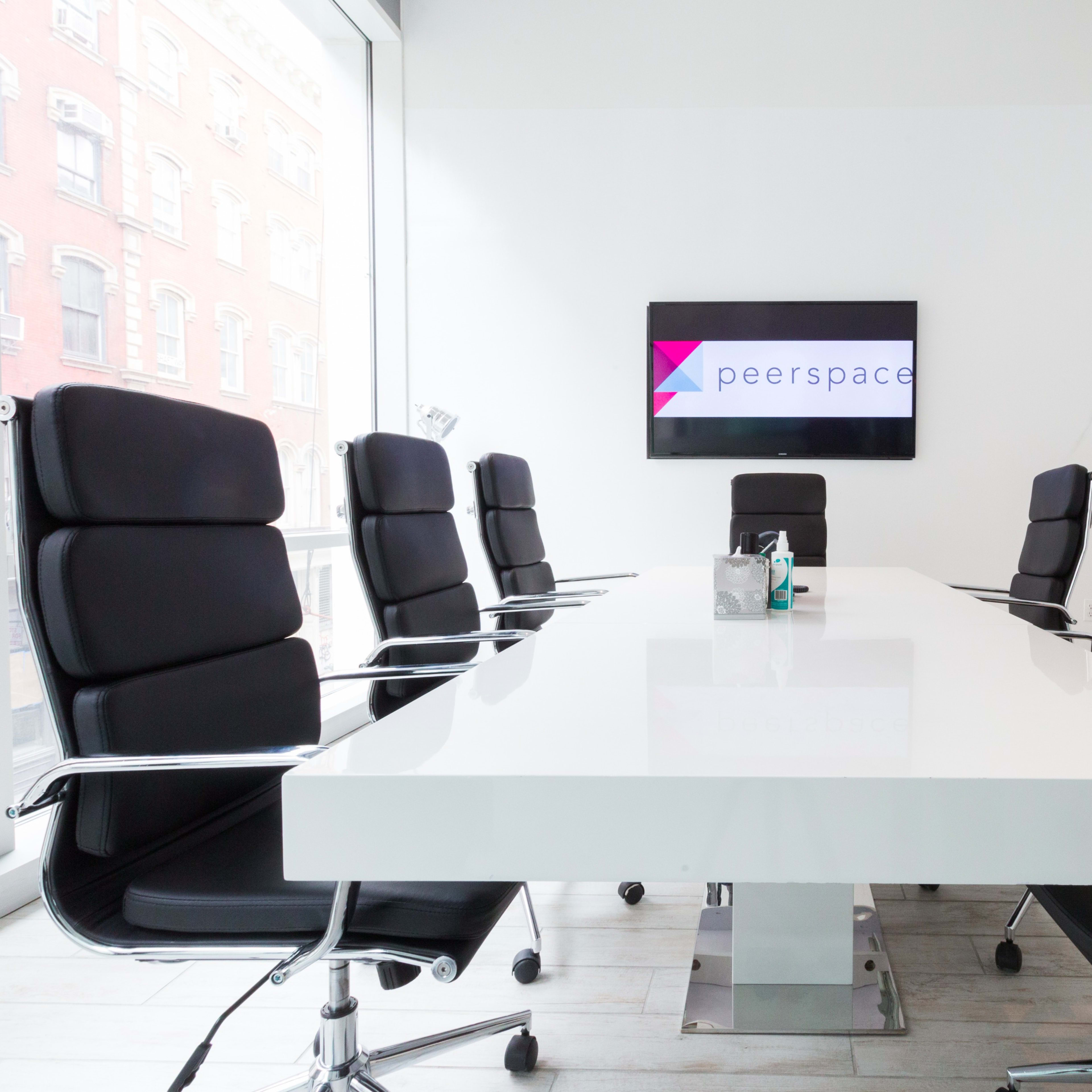 A modern conference room features a long white table surrounded by black ergonomic chairs, with a large screen displaying the Peerspace logo on the wall.