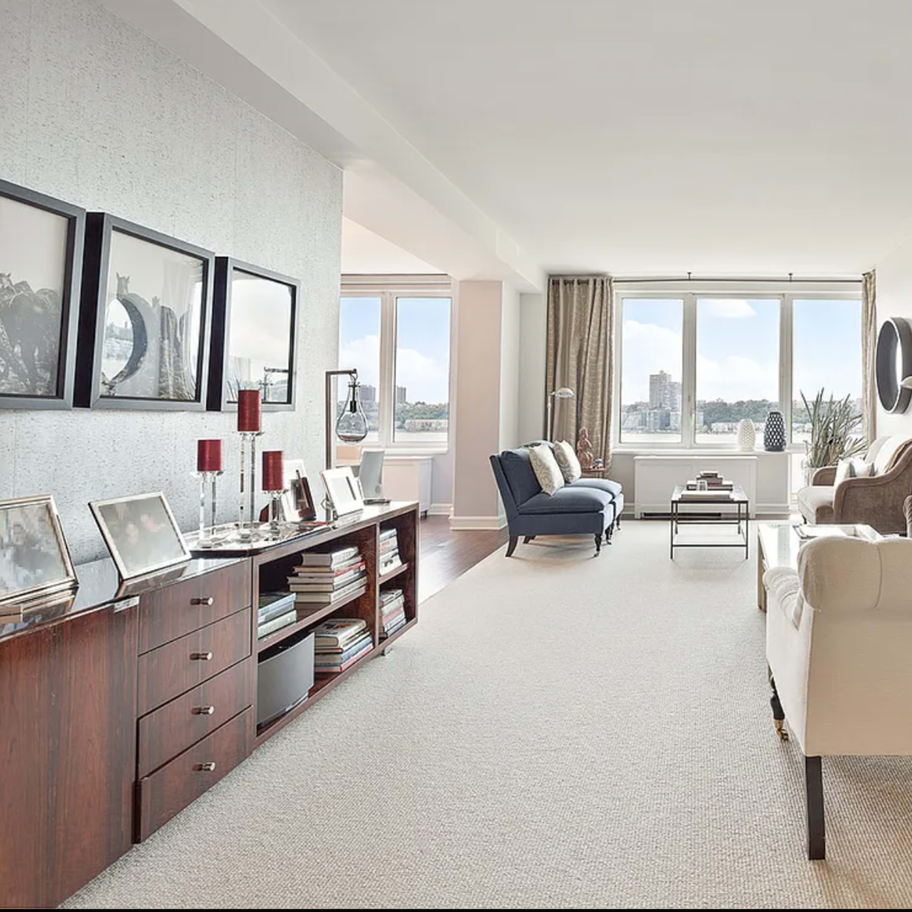 A modern living room with a light-colored carpet, two sofas, a coffee table, and large windows offering a view of the outdoors.