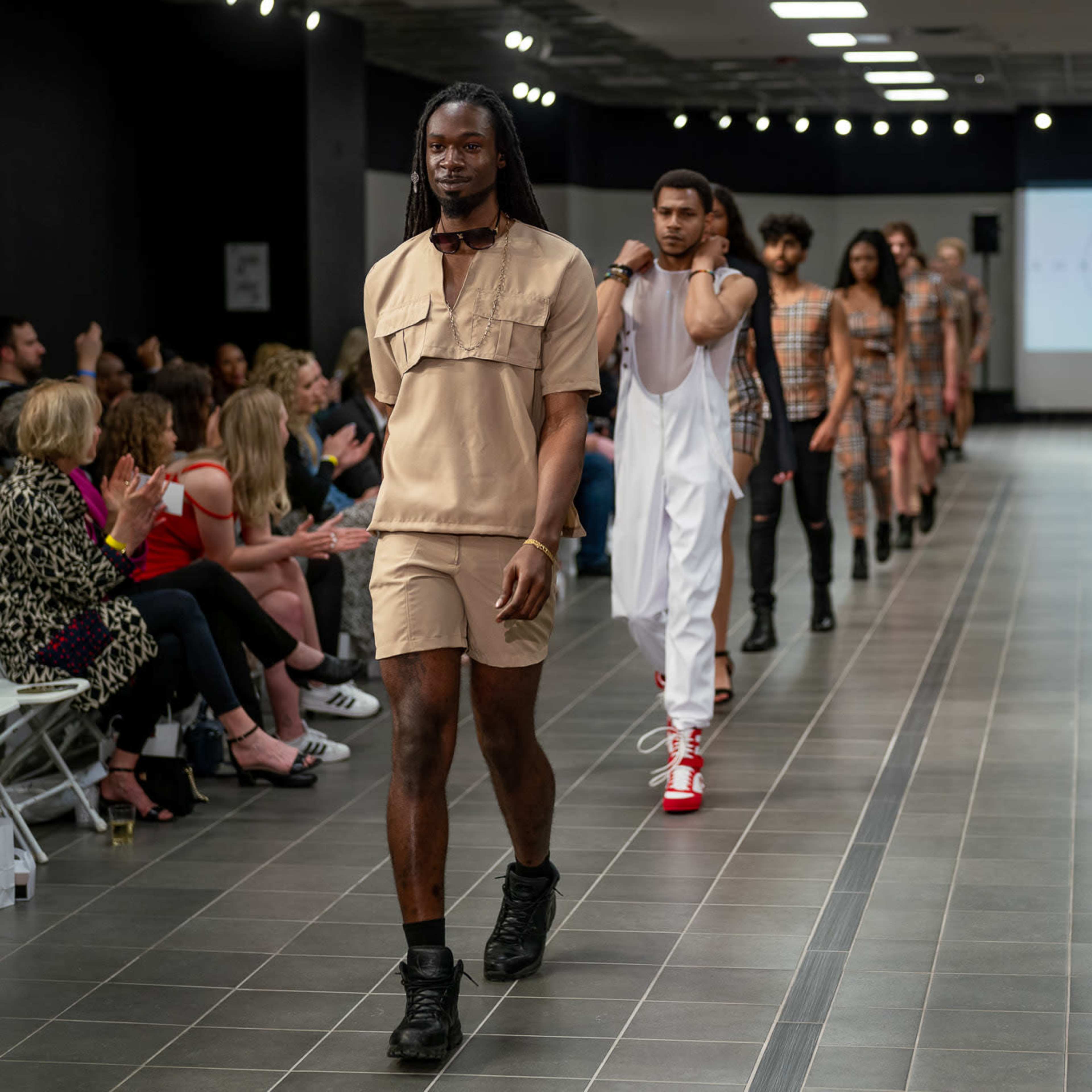 Models walk down a runway during a fashion show, showcasing a variety of apparel styles.