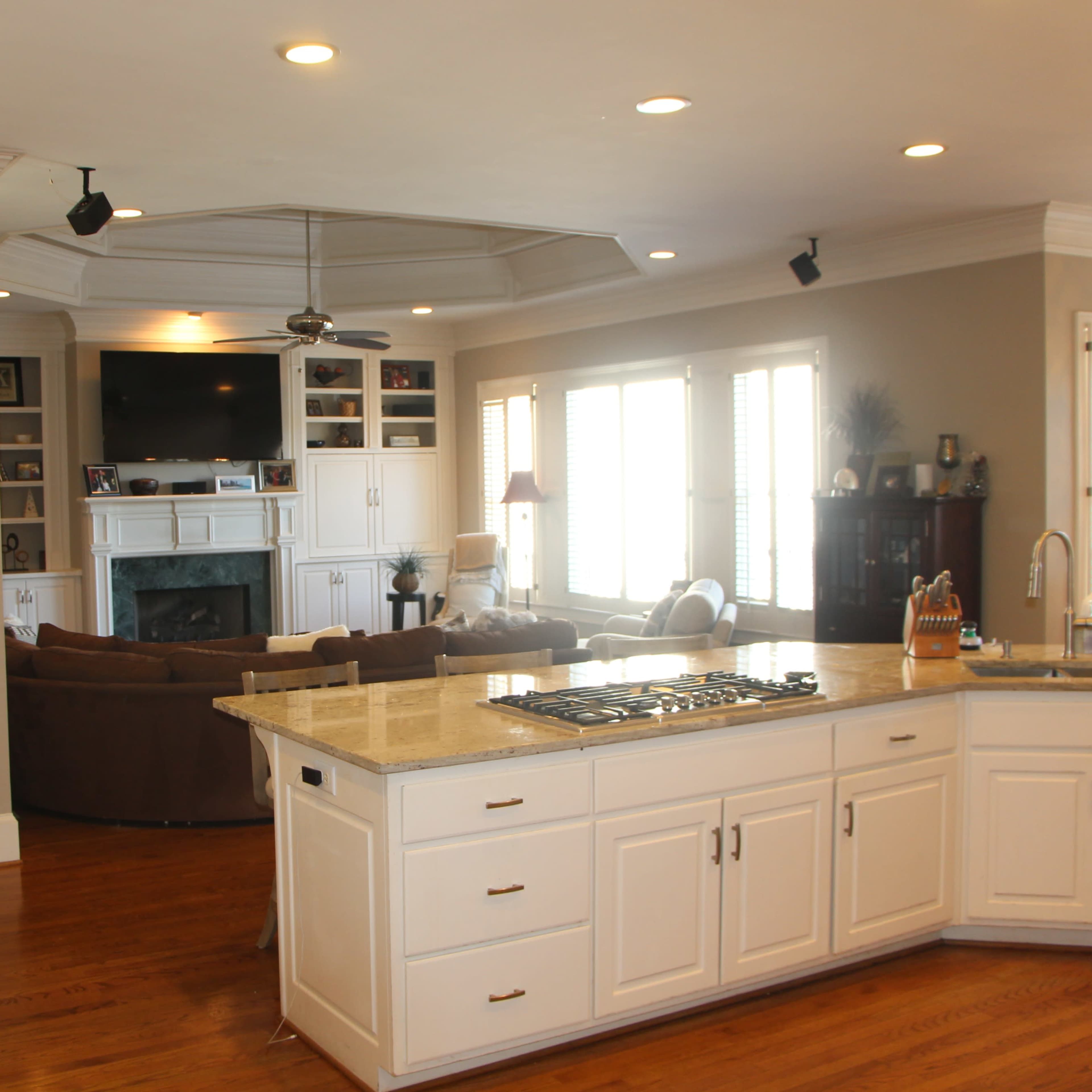 A kitchen with white cabinetry and a gas stove, overlooking a living area with a television and sectional seating.
