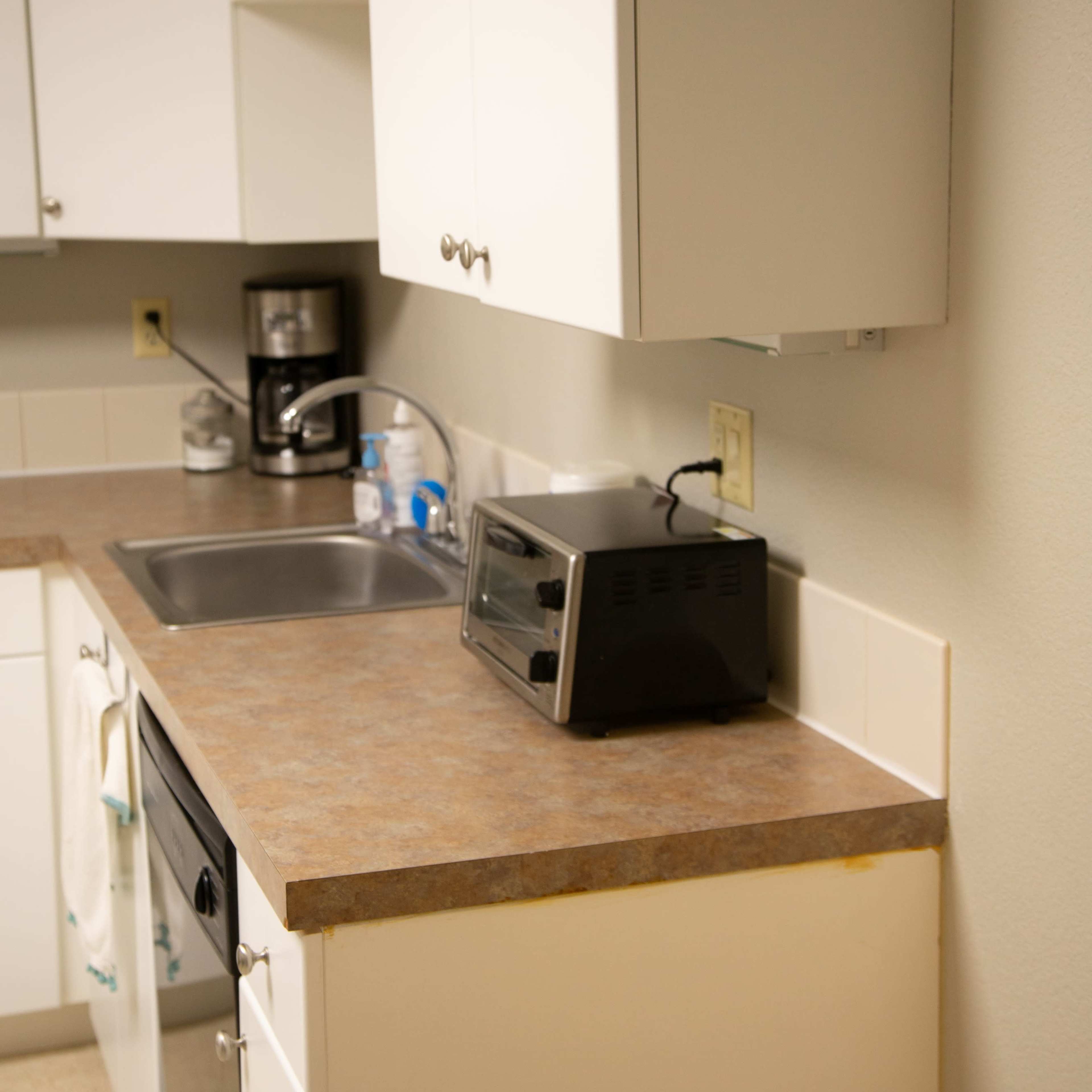 A kitchen with white cabinetry, a stainless steel sink, a toaster, and a coffee maker on the countertop.