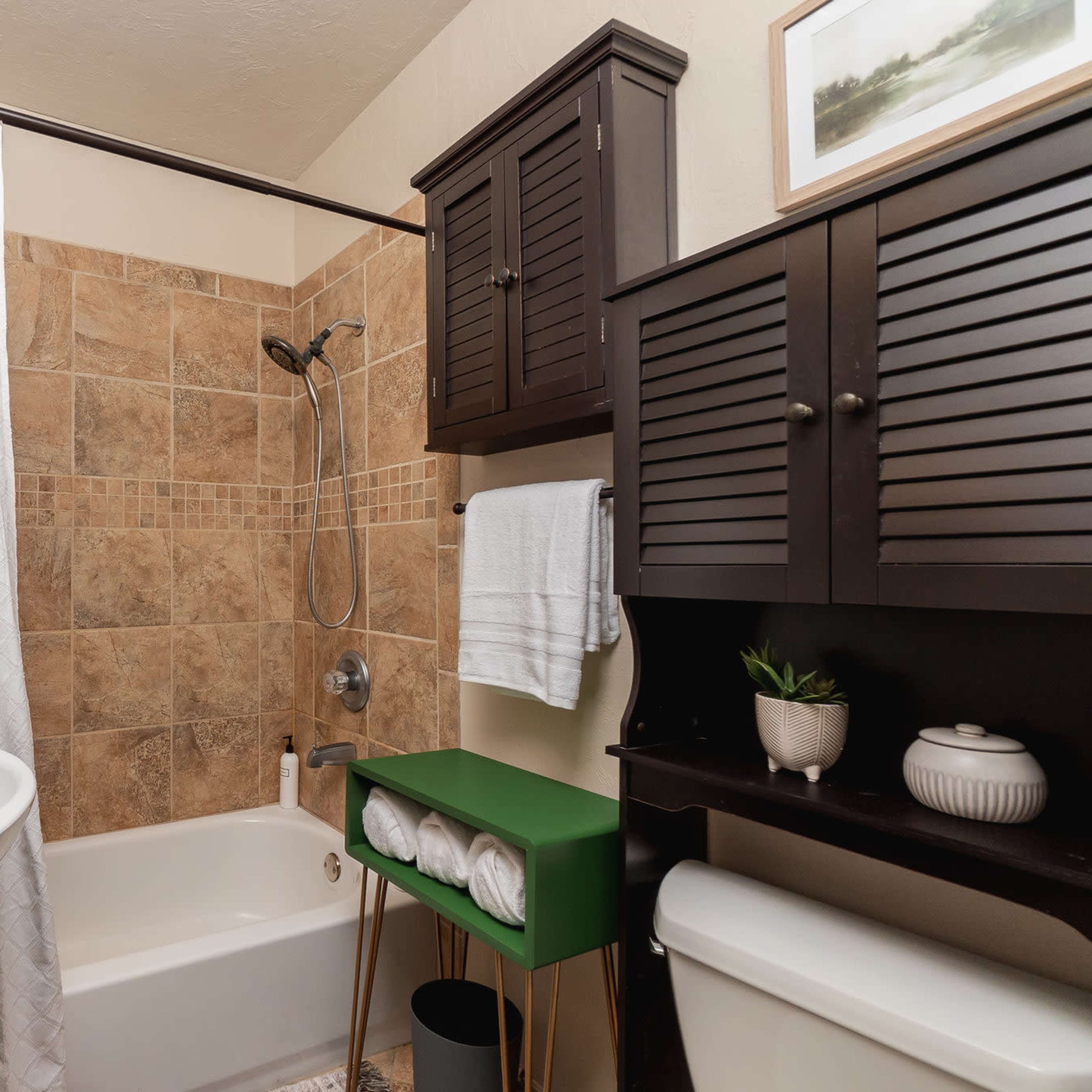 A small bathroom featuring a bathtub with a shower, a storage cabinet, and a towel rack, all enclosed in tiled walls.