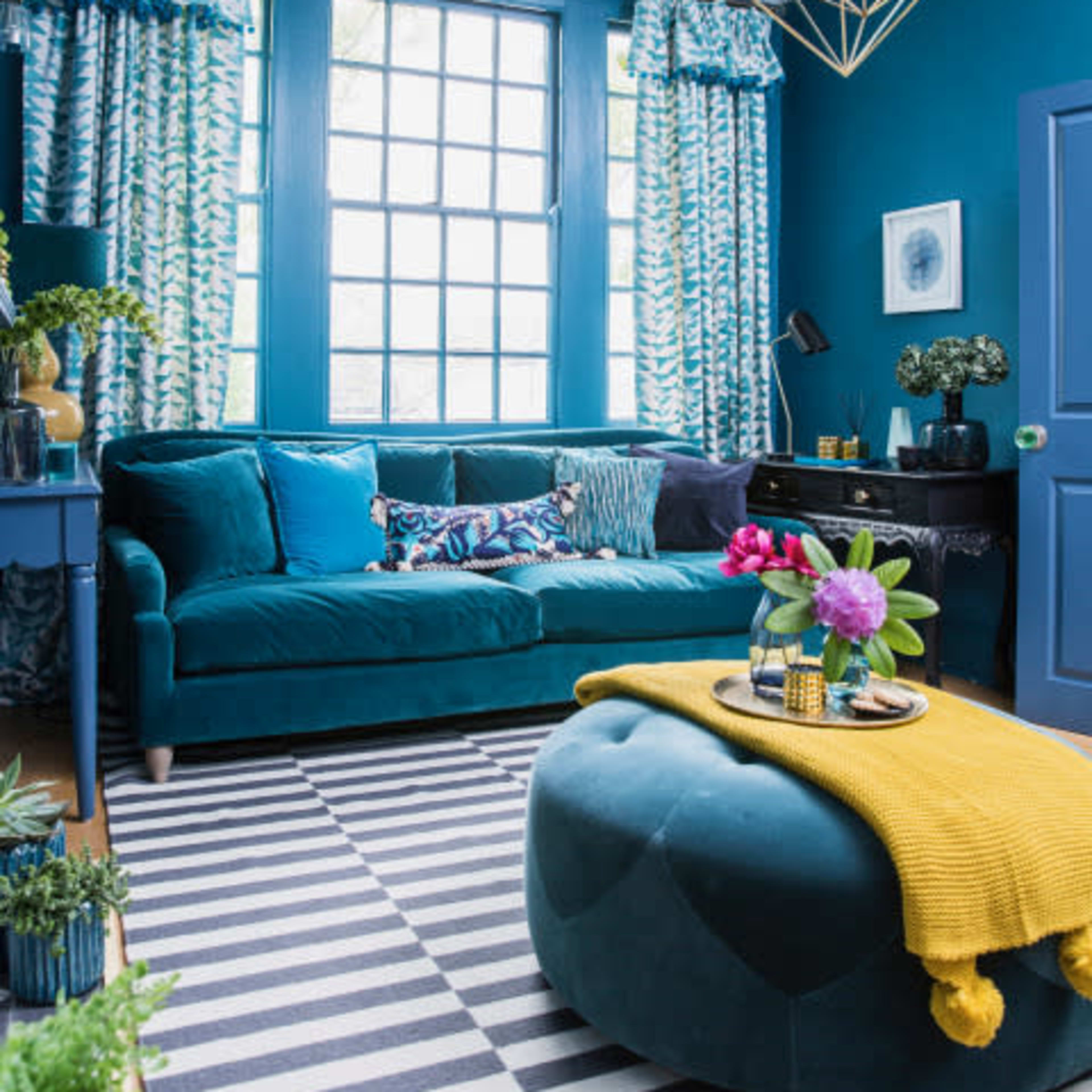 A brightly colored living room featuring a teal sofa, patterned curtains, a striped rug, and decorative plants.