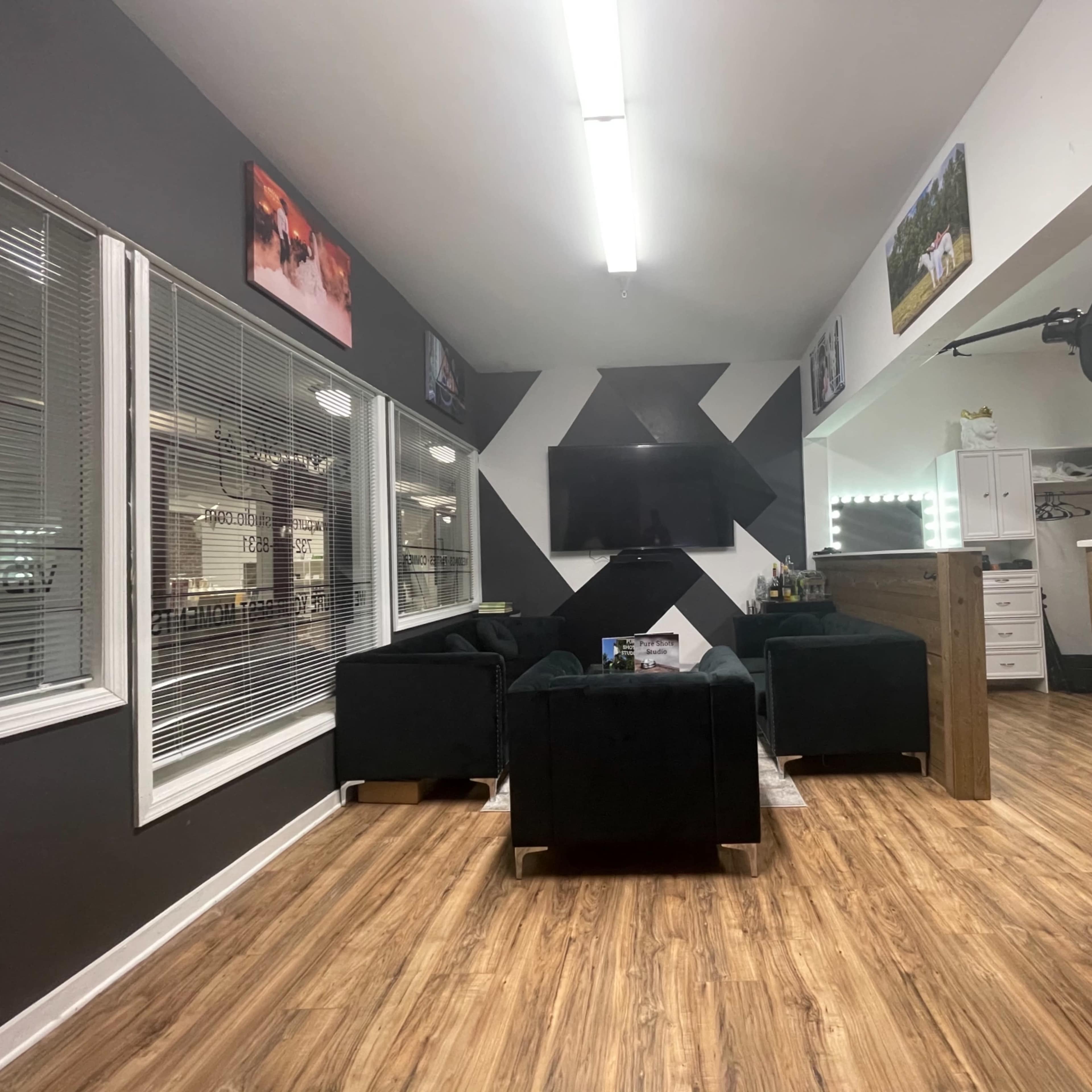 A modern lounge area with black furniture, a large wall-mounted television, and decorative wall art in a bright room with wood flooring.