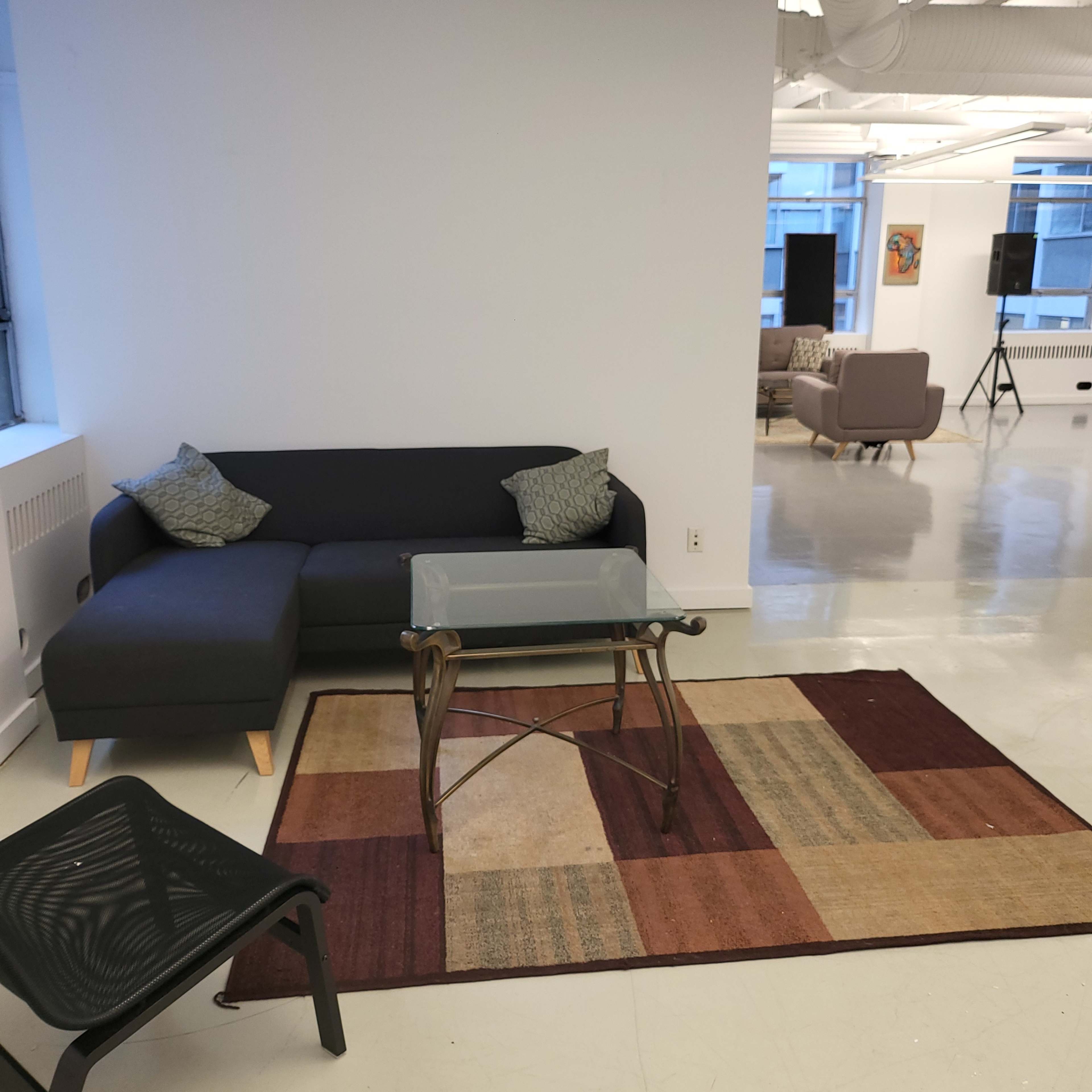 A modern lounge area with a dark sectional sofa, a glass coffee table, and a patterned rug on the floor.