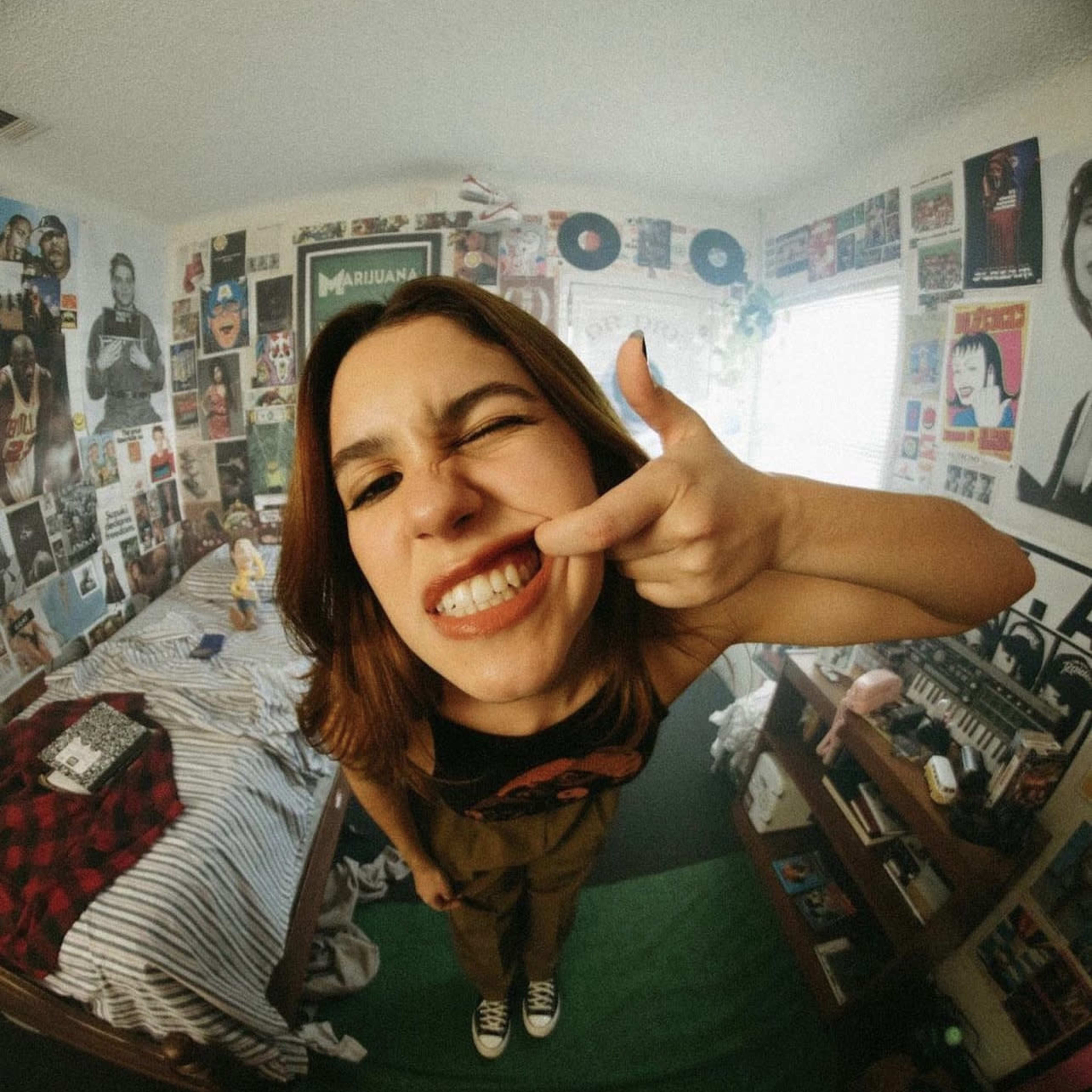 A person makes a playful gesture with their hand in a bedroom filled with music posters and various decorations.
