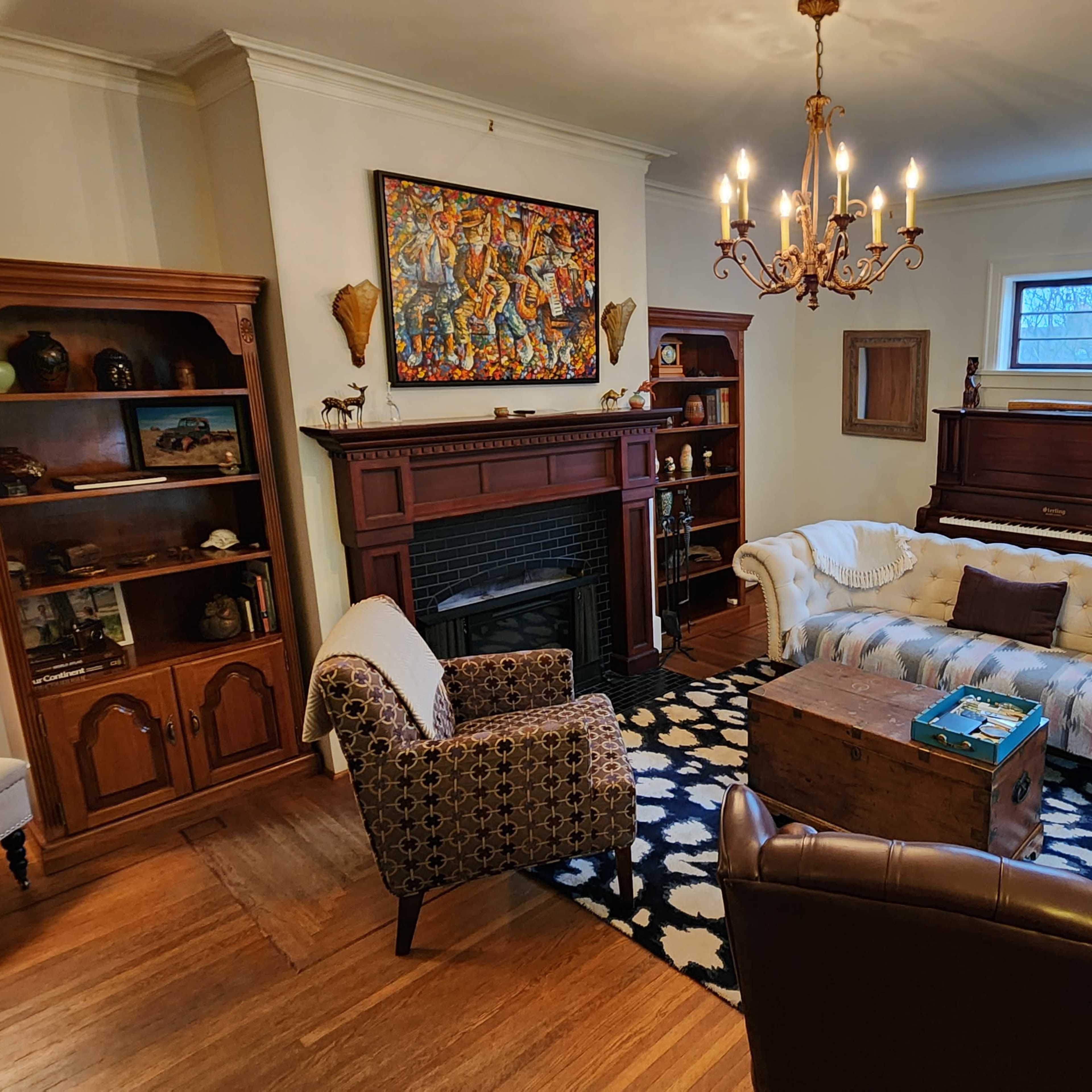 A cozy living room features a white tufted sofa, a wooden coffee table, and two armchairs, surrounded by bookshelves and art on the walls.