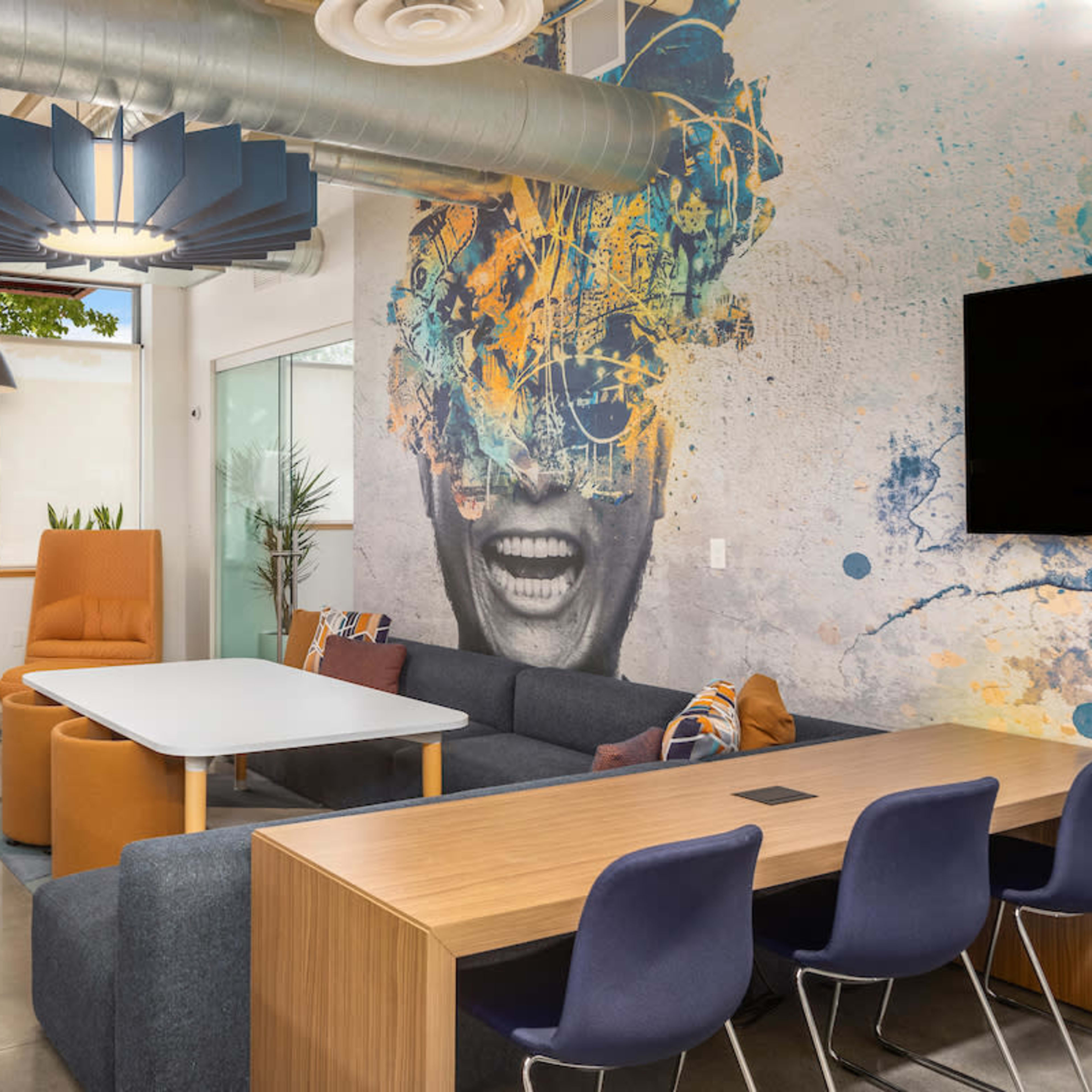 A modern lounge area featuring a large sofa, colorful chairs, a table, and a vibrant mural on the wall.