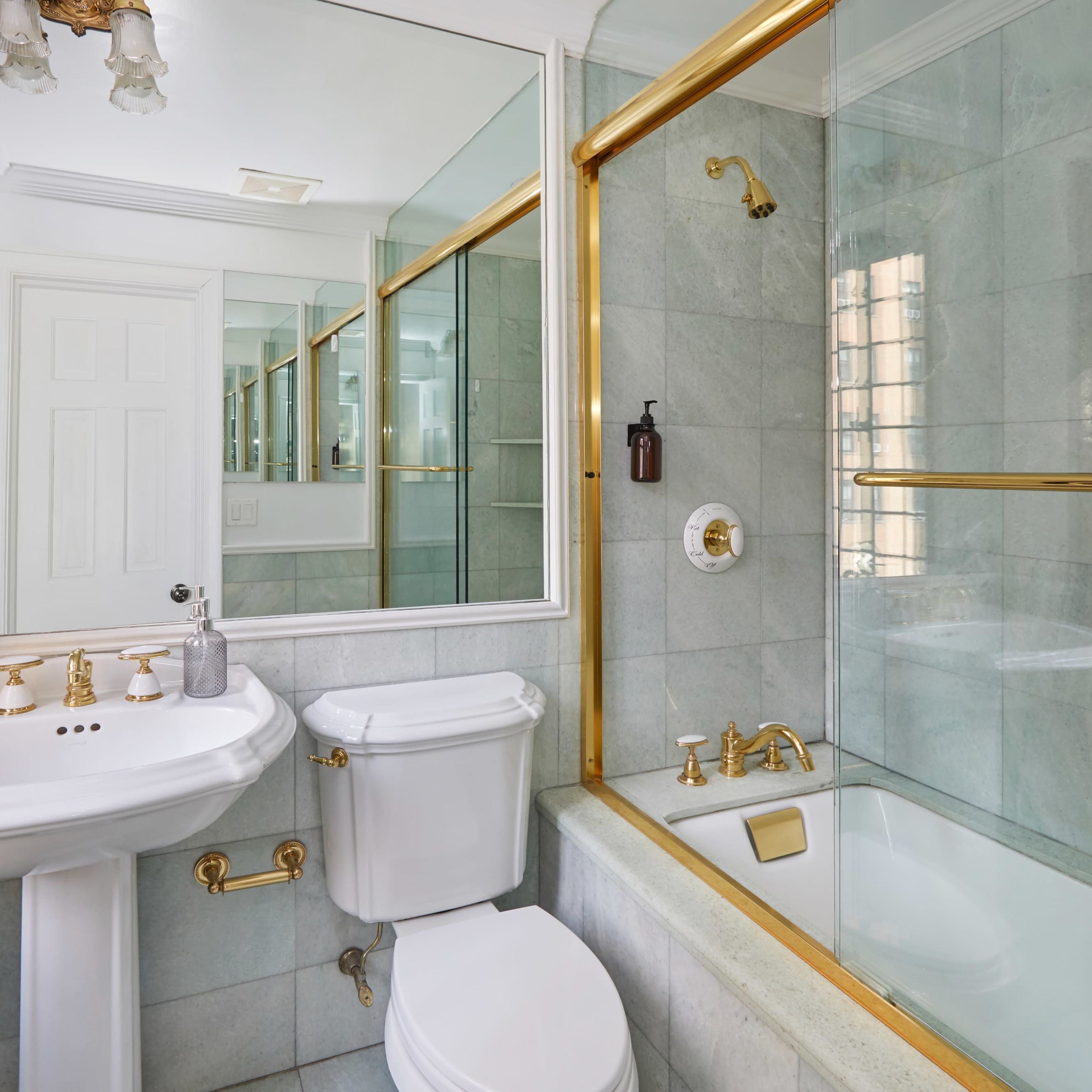 A bathroom featuring a pedestal sink, a toilet, a bathtub with a glass shower enclosure, and mirrored cabinets.