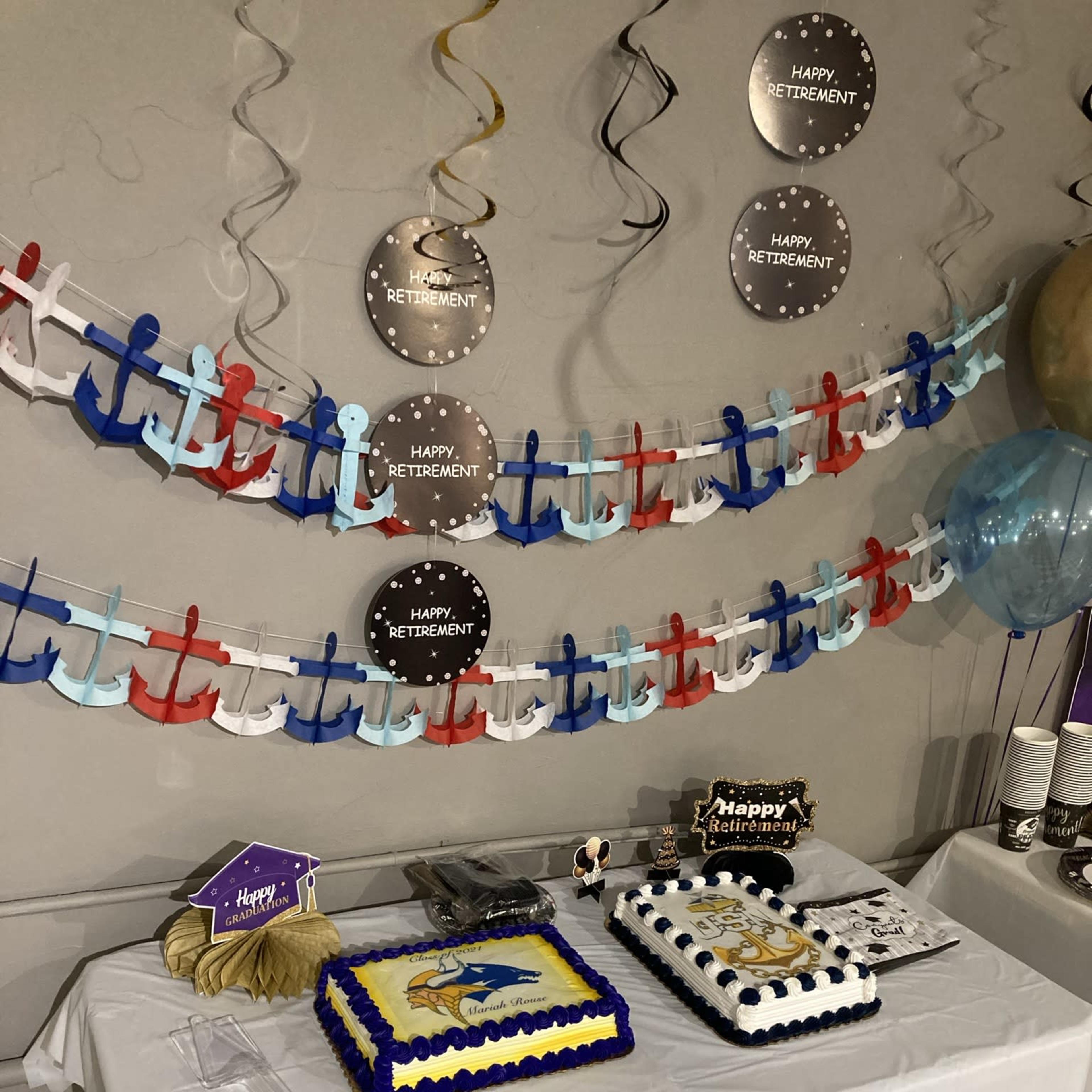 A decorated table features two retirement-themed cakes, along with festive decorations including banners and balloons.
