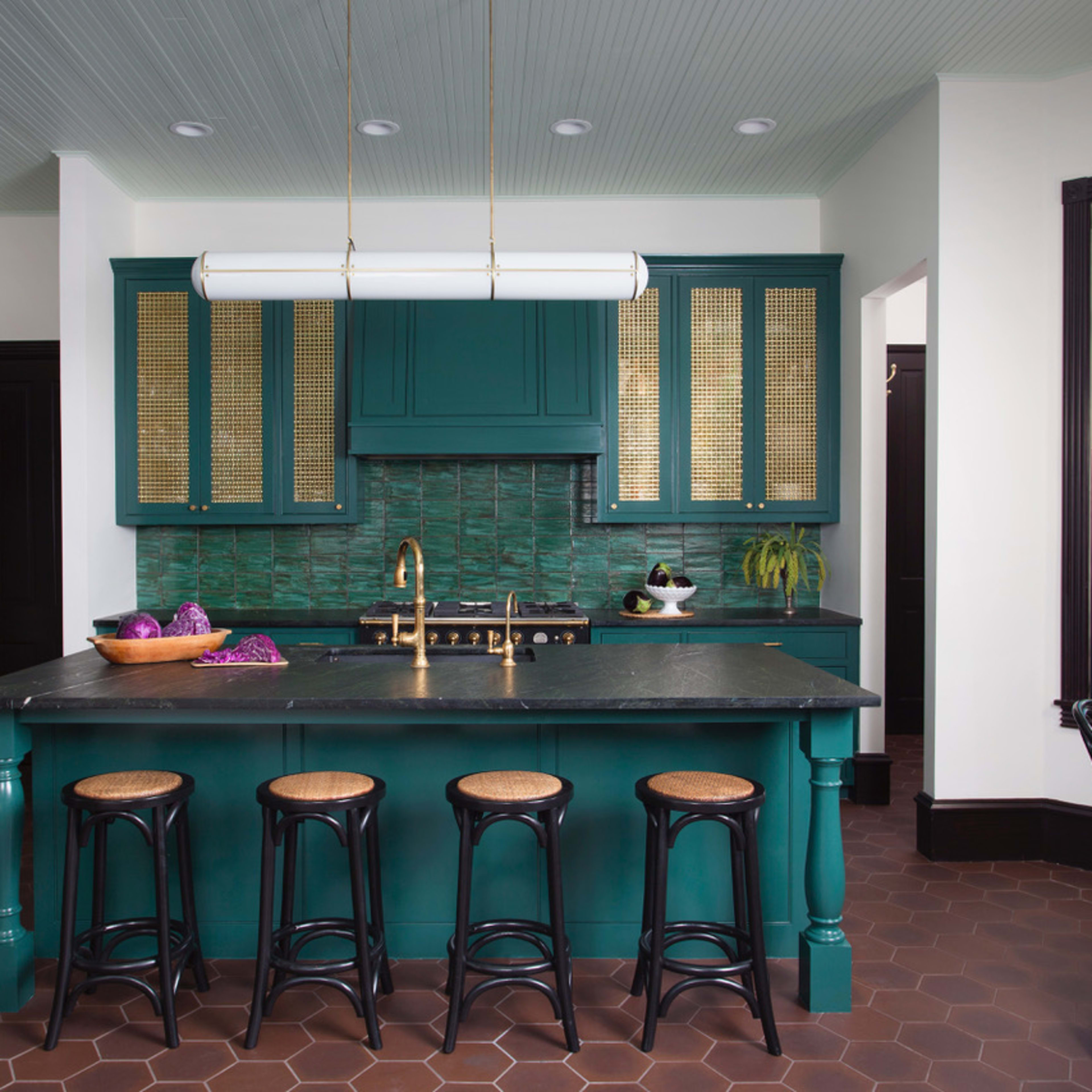 The kitchen features a large teal island with four black stools, a brass faucet, and green tile backsplash, surrounded by white walls and dark trim.