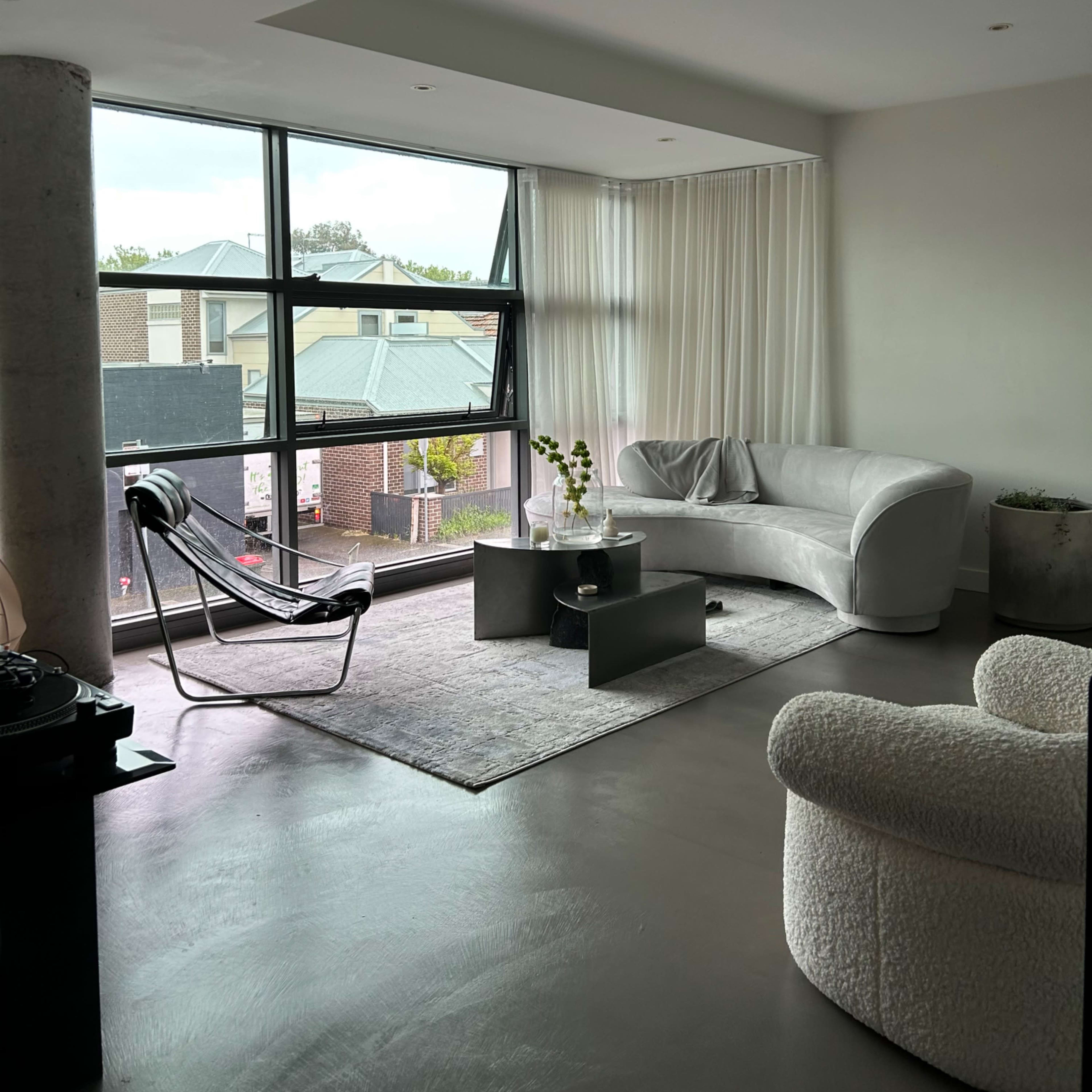A modern living room with a large window, light-colored furniture, and a minimalist decor style.