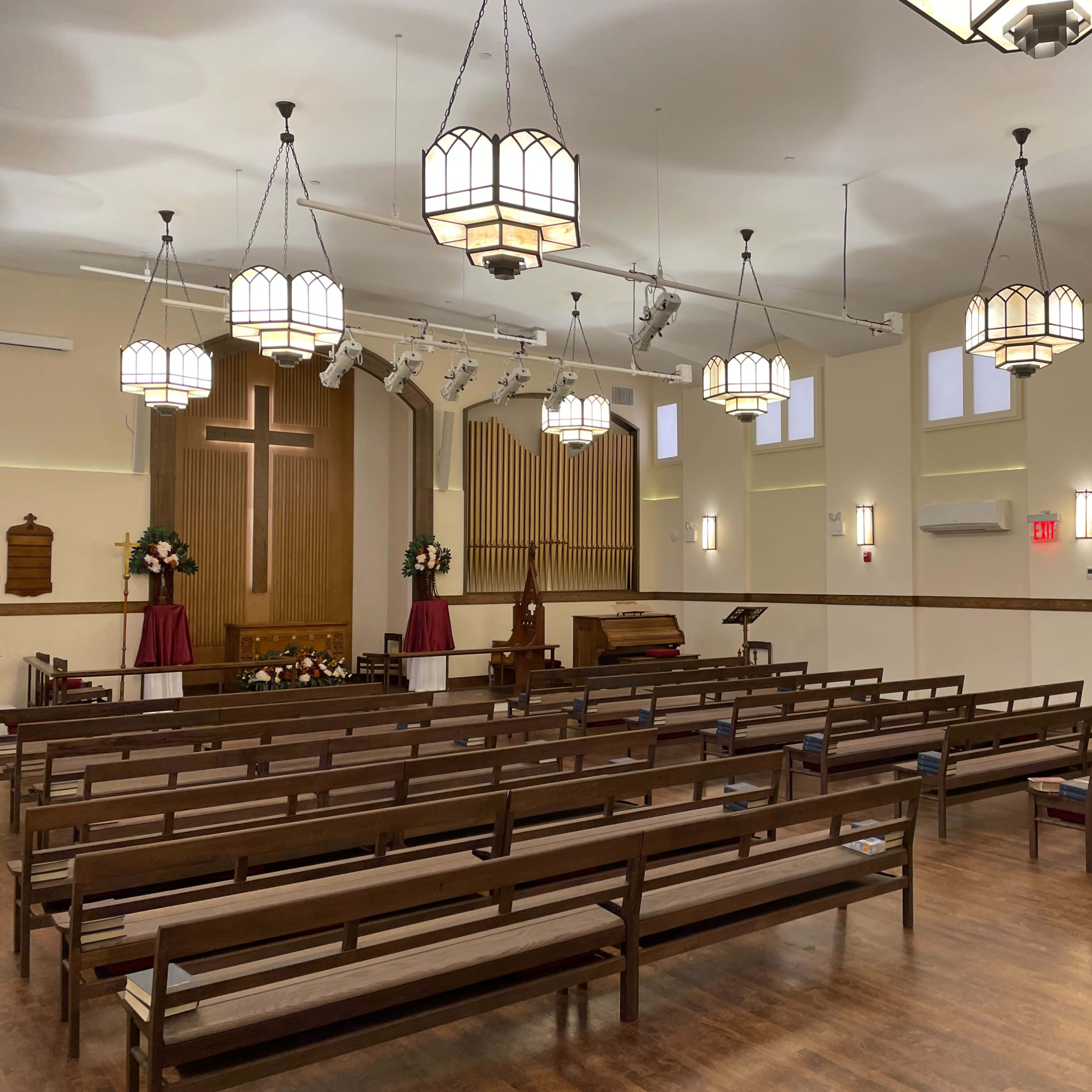 A spacious church interior with wooden pews arranged facing a front stage that has a large cross and an organ.