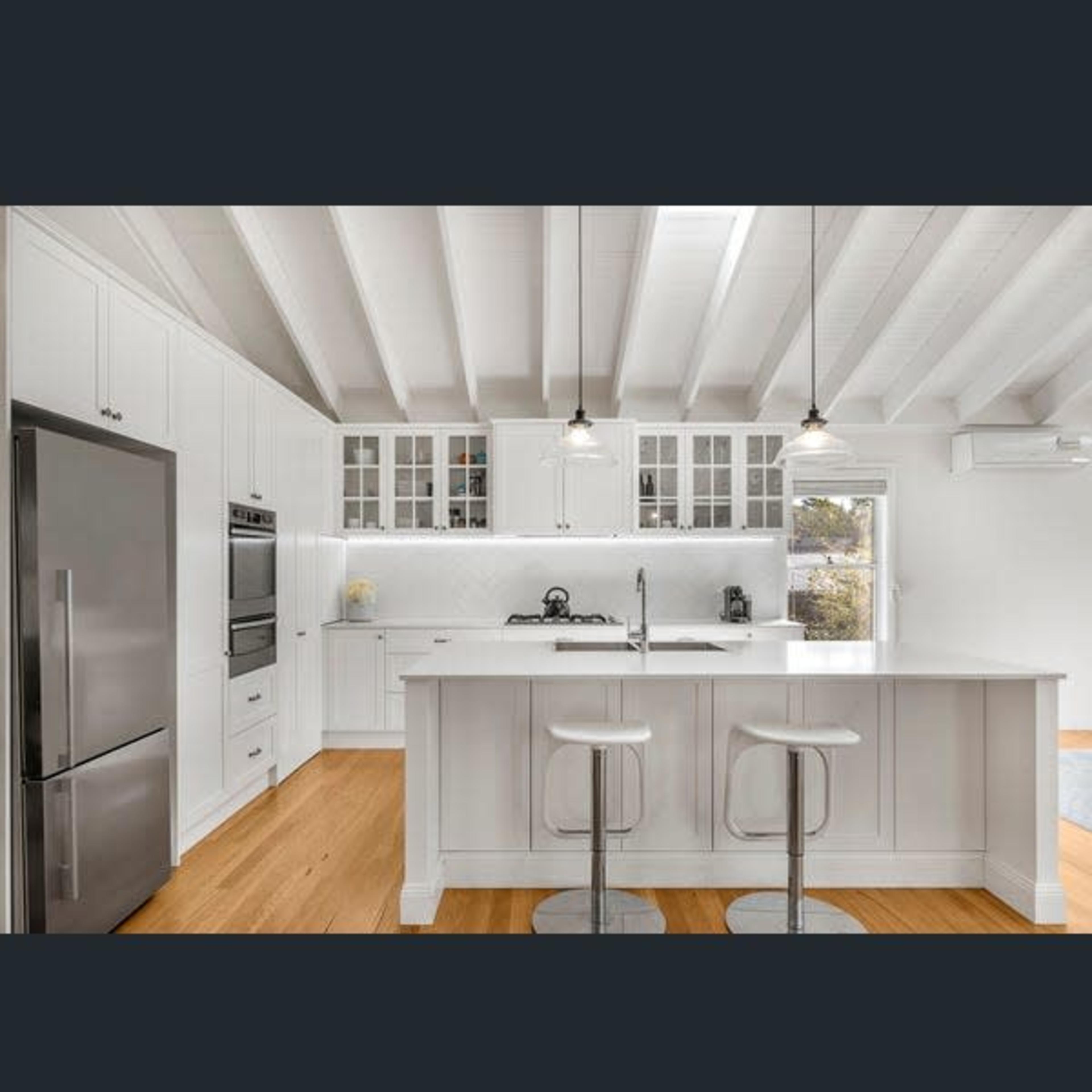 A modern kitchen with white cabinetry, stainless steel appliances, and a central island with two stools.