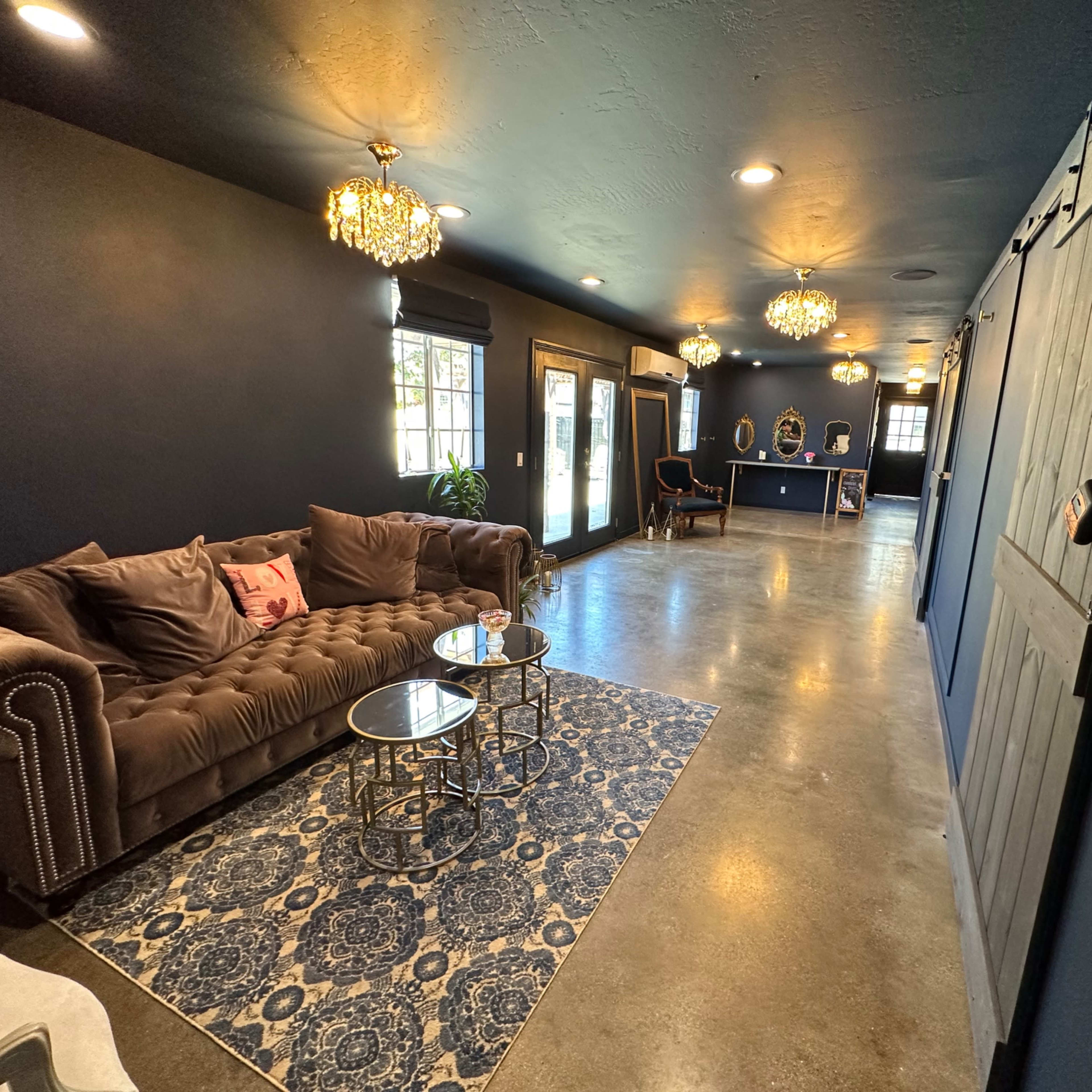 A cozy interior space with a velvet sofa, decorative lighting, and a patterned rug, leading to a counter area at the end.