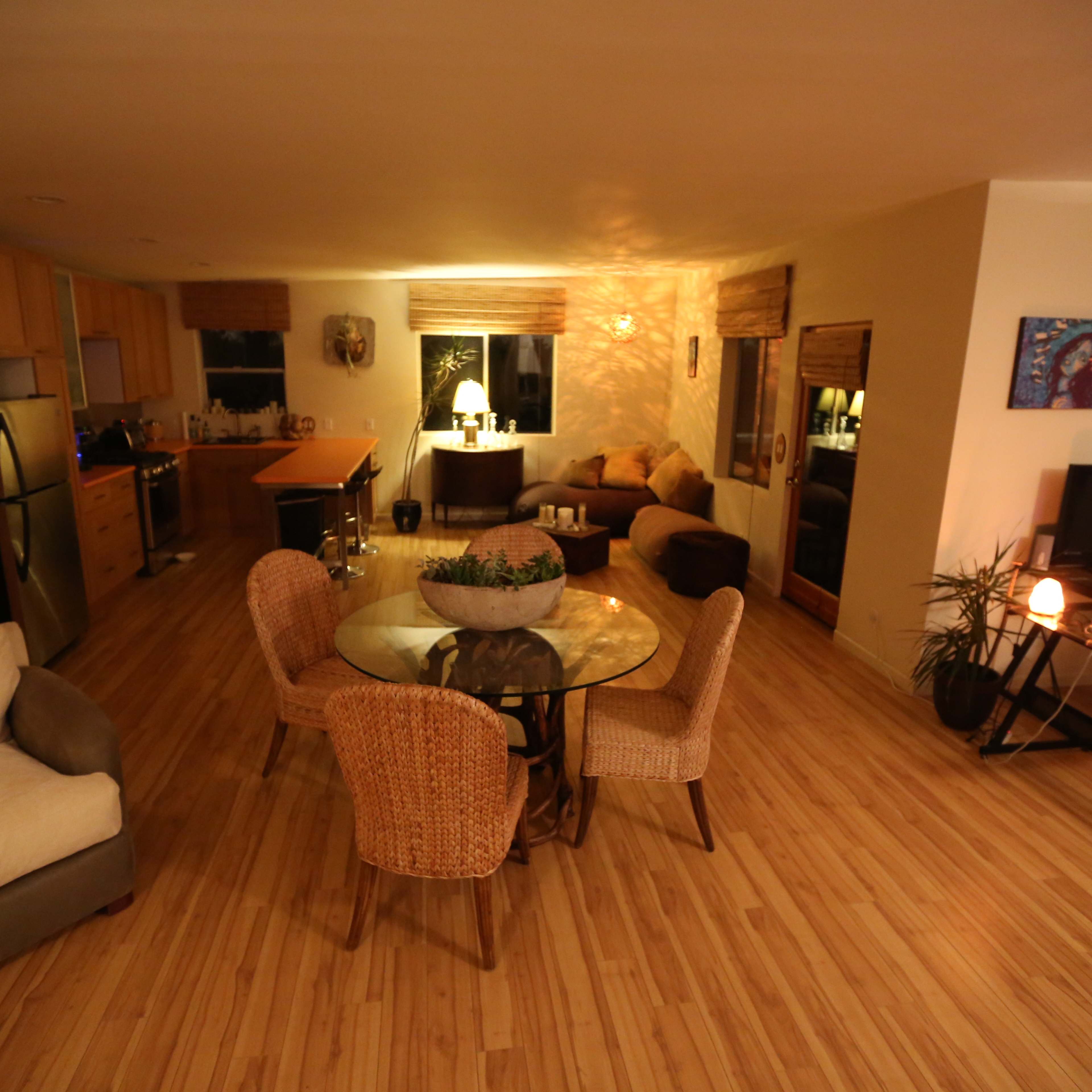 The scene depicts a spacious living area featuring a dining table with chairs, a sofa, and several seating areas, all illuminated by soft lighting.