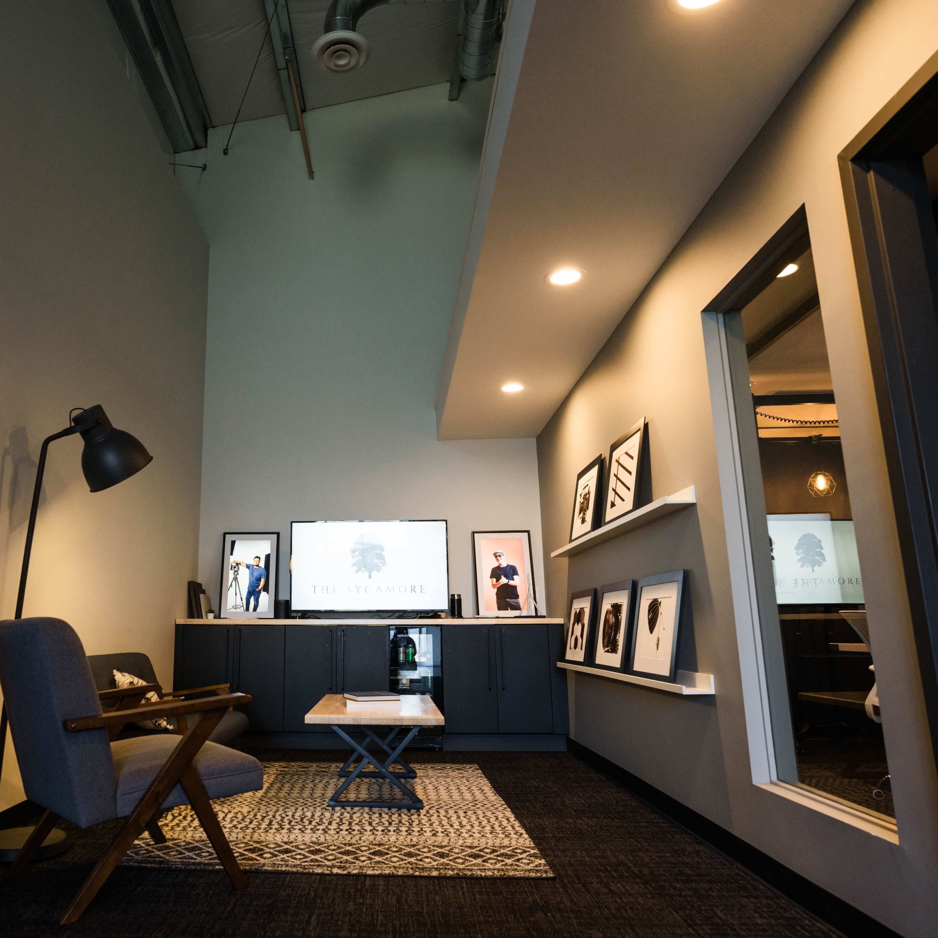 A modern office space with a decorative shelving unit, a gray armchair, a coffee table, and a television displaying a logo on the wall.