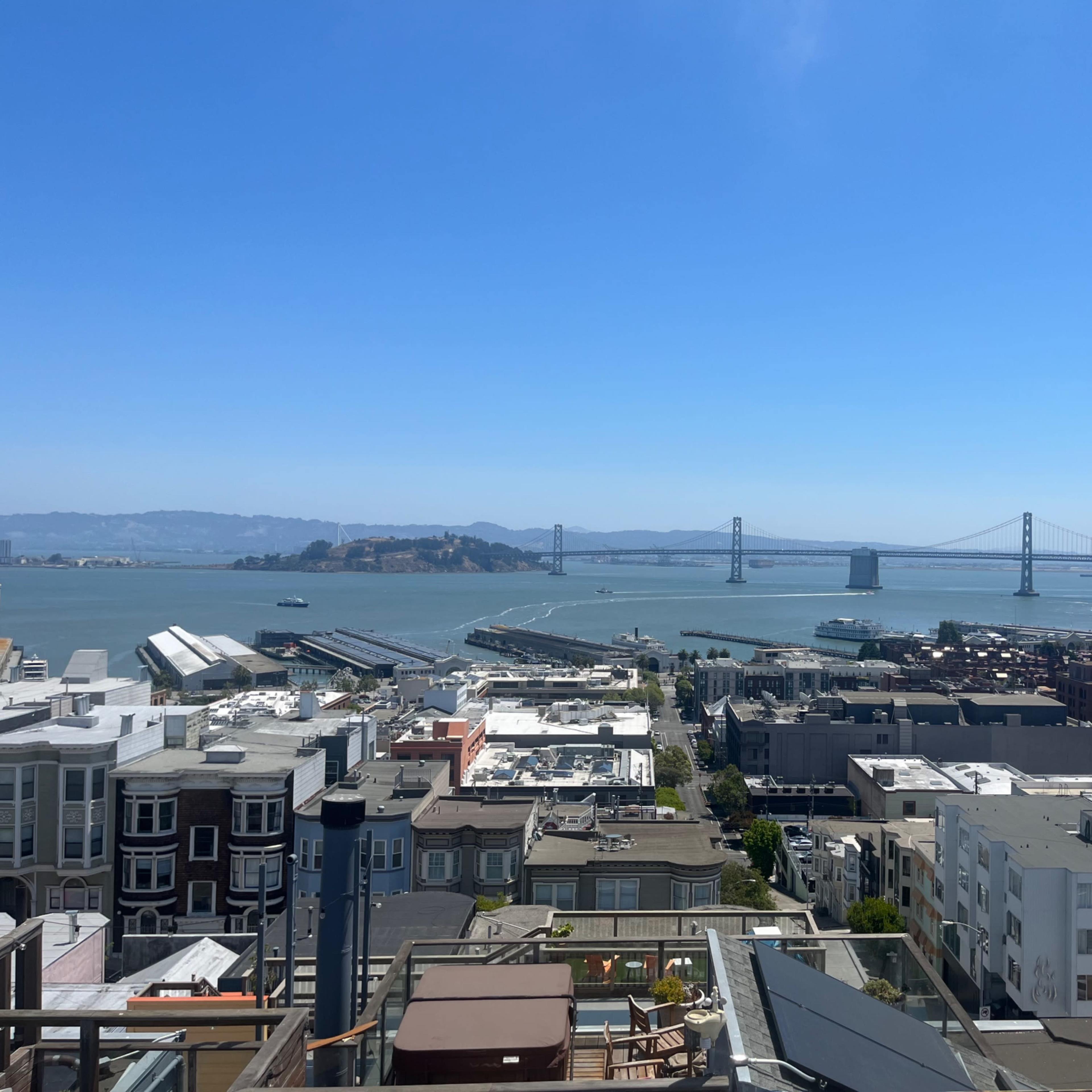 A panoramic view of San Francisco Bay, featuring the Bay Bridge in the distance and a cluster of buildings in the foreground.