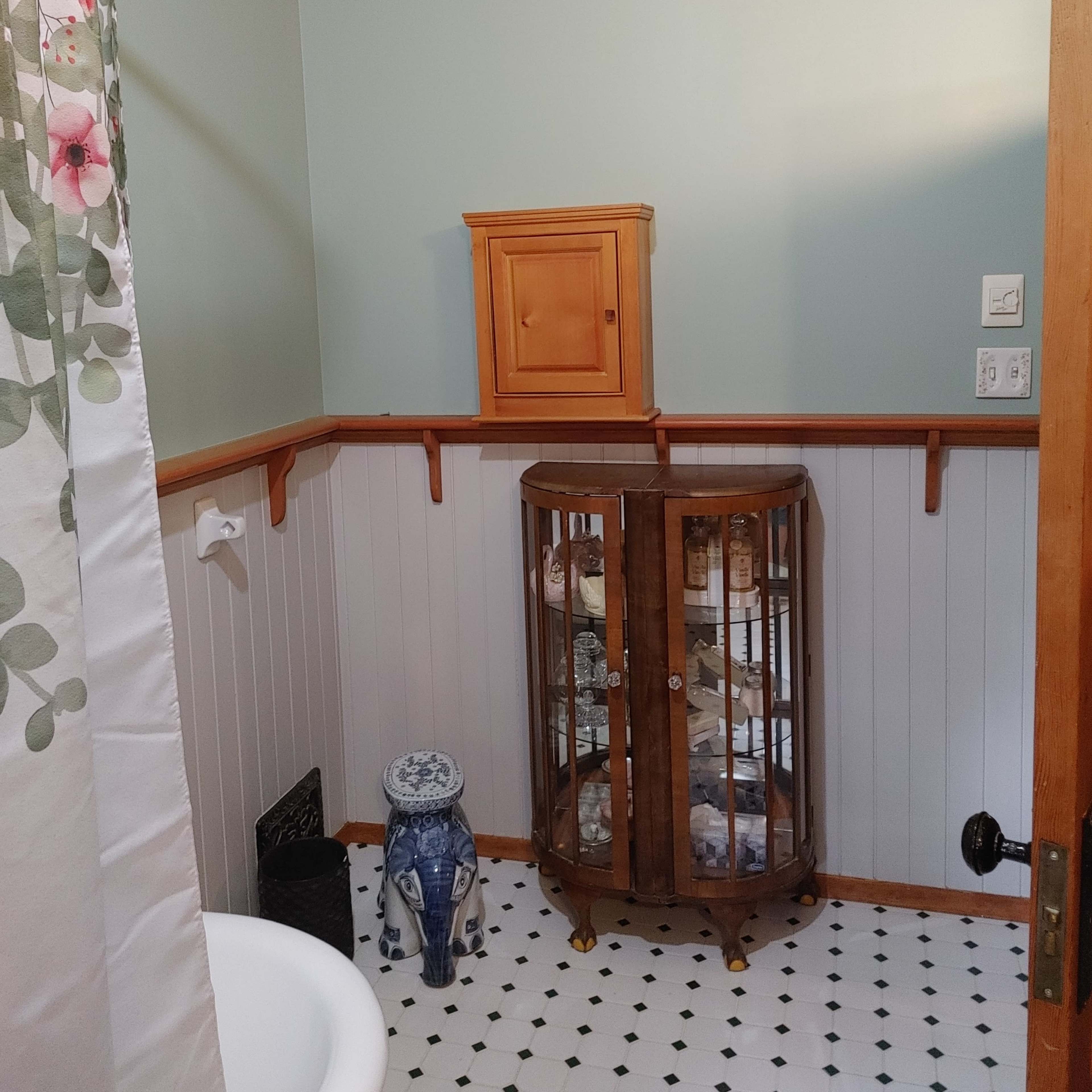 A small bathroom with a clawfoot bathtub, a wooden display cabinet, and light green walls.